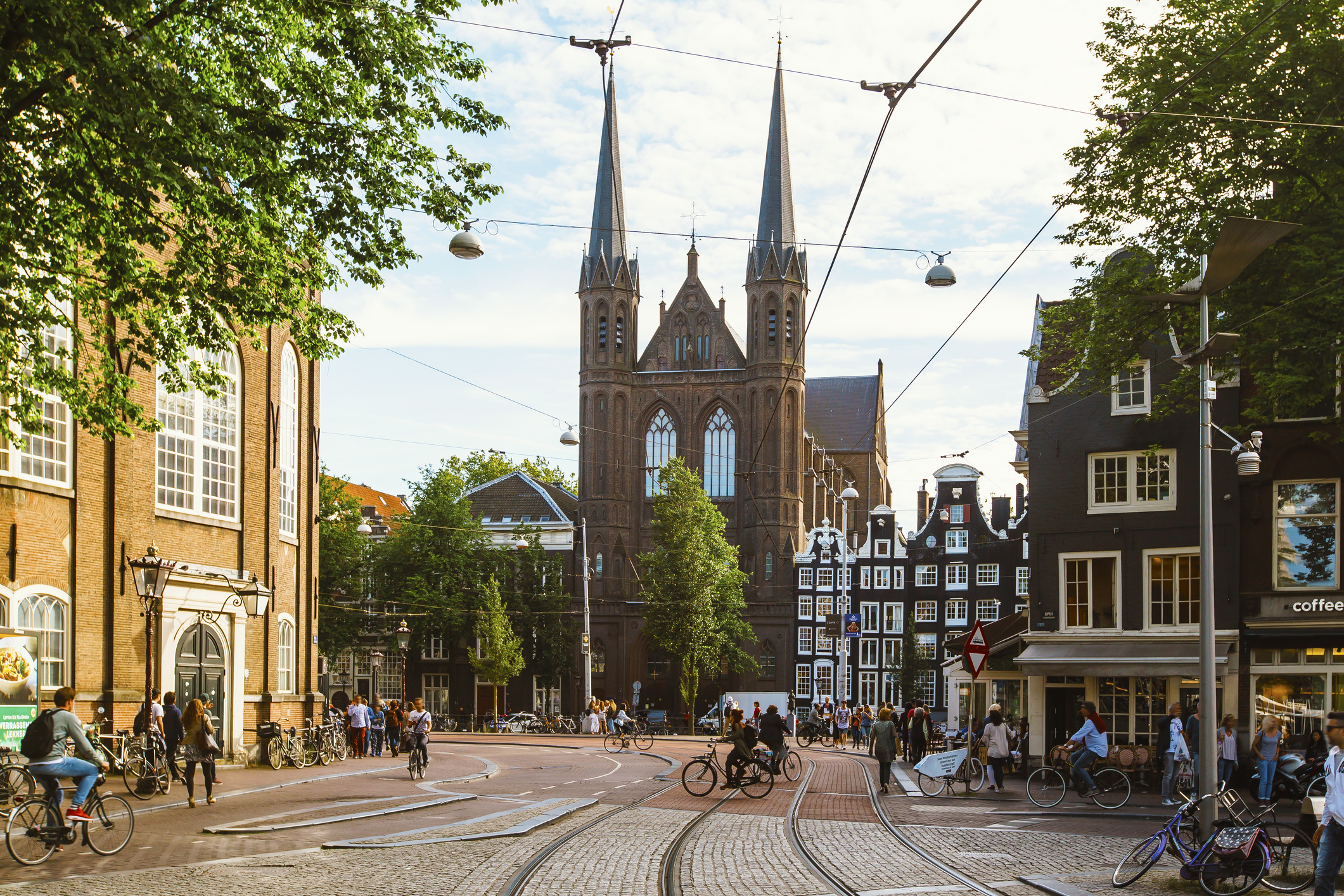 Street view with people cycling and walking, historical buildings, and a church with twin spires