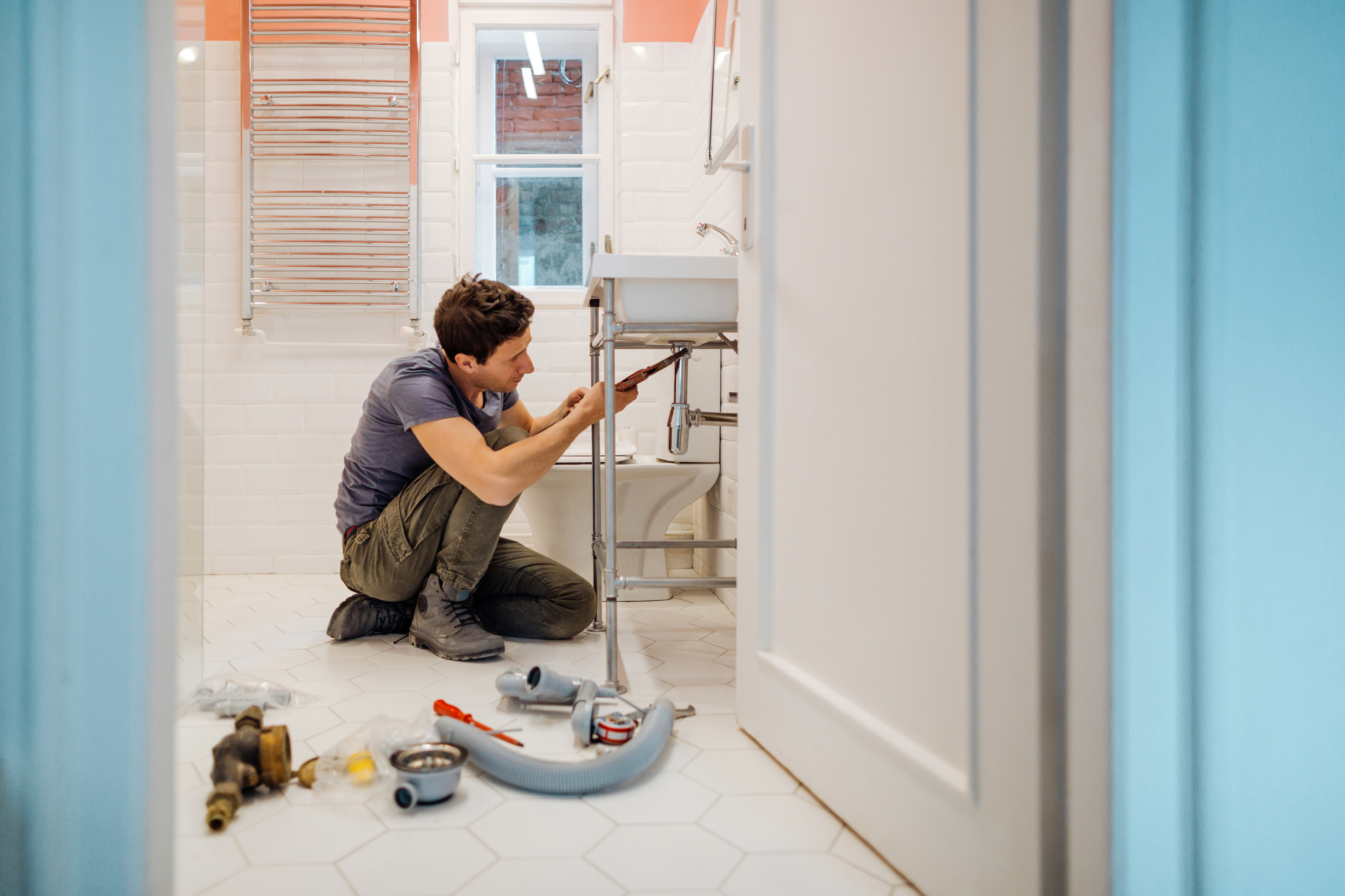 Person repairing sink pipes in bathroom, tools scattered around on the floor