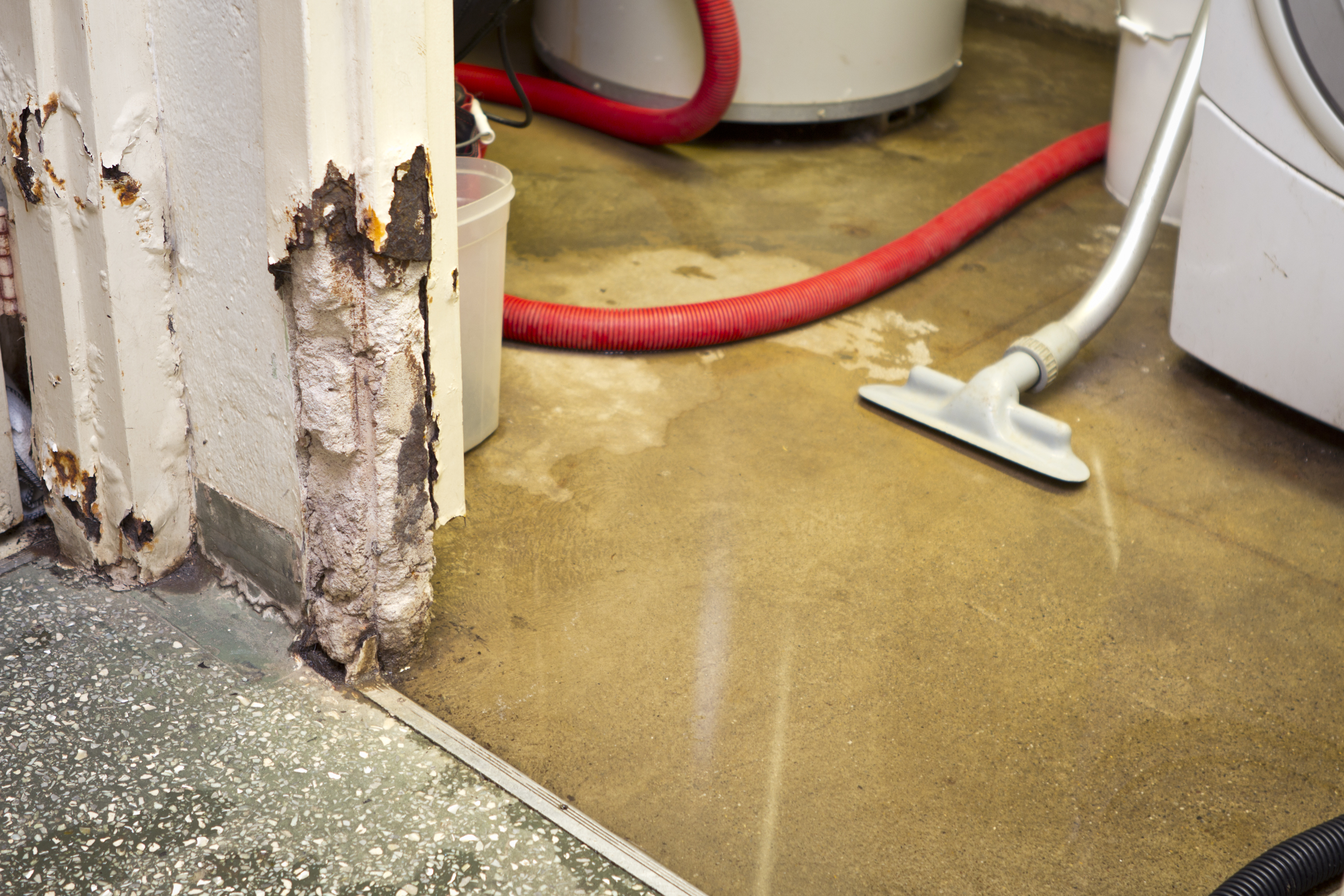 A flooded room with a vacuum cleaner sucking up water, showing water damage on the wall