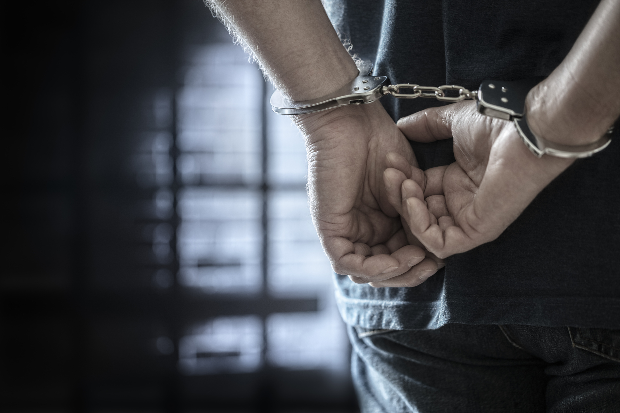 A person is handcuffed with their hands behind their back in a dimly lit room