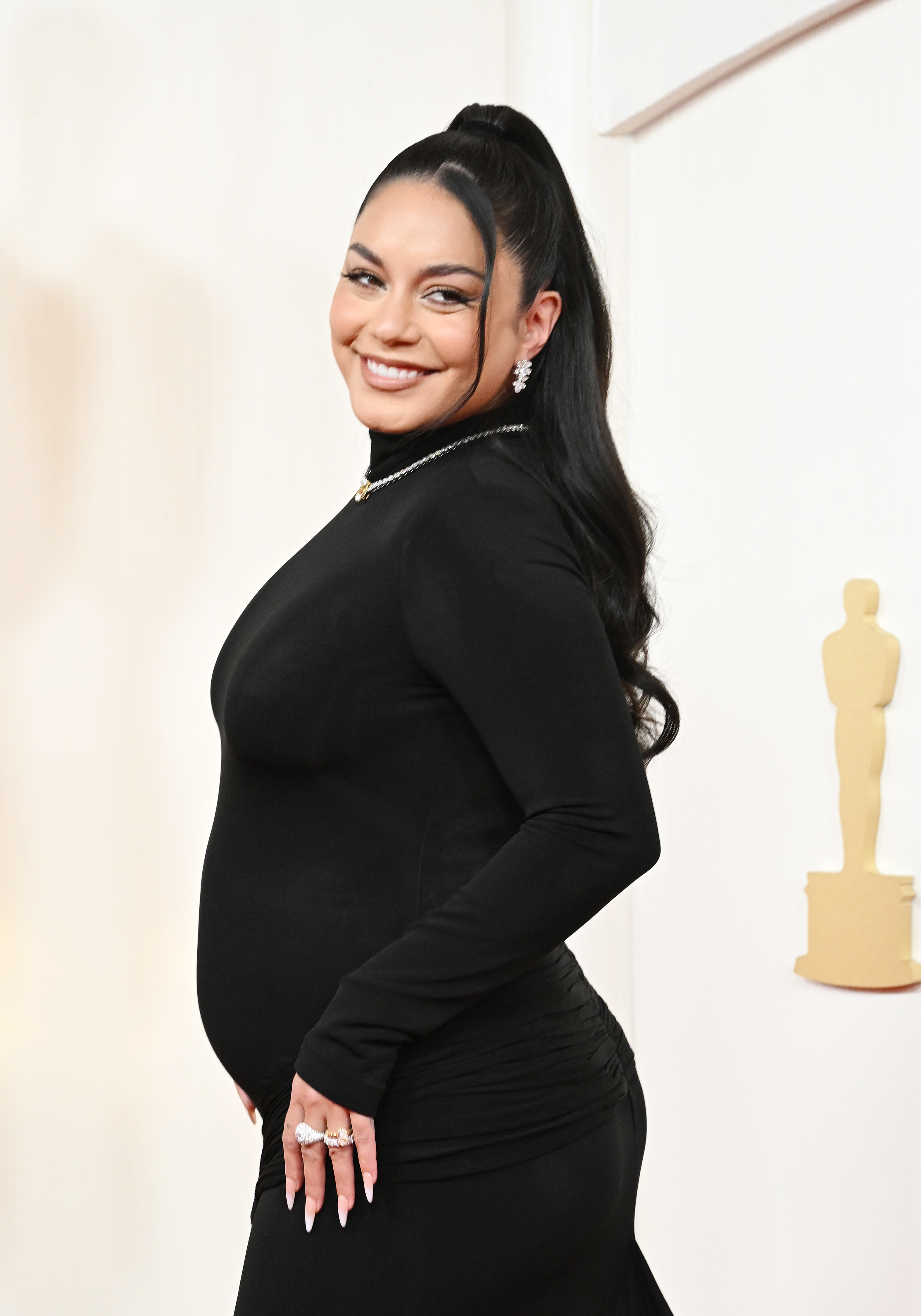 Vanessa Hudgens in a black dress at an event, posing with her hand on her hip