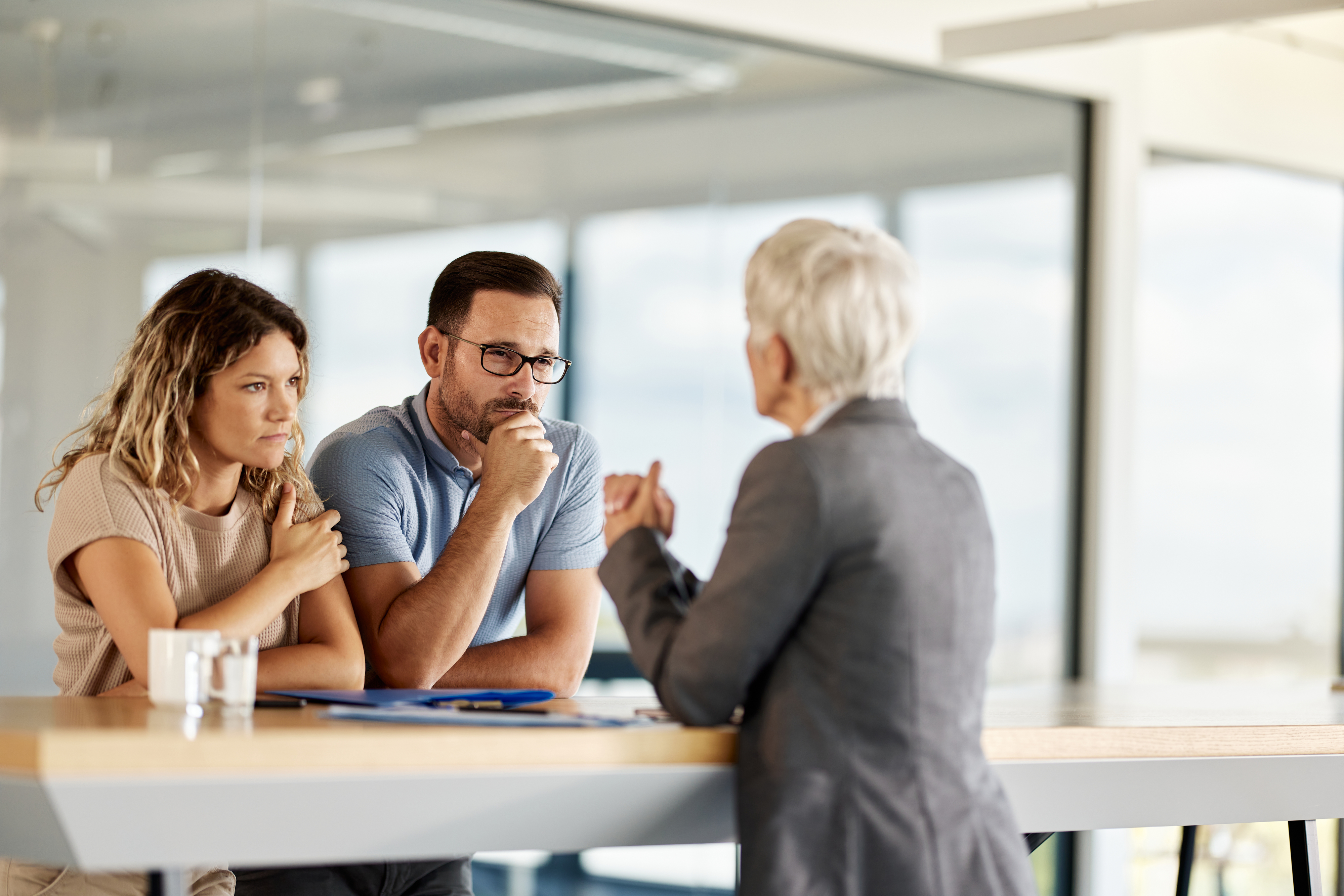 Two individuals consulting with a professional at a desk, showing concern and engagement in conversation