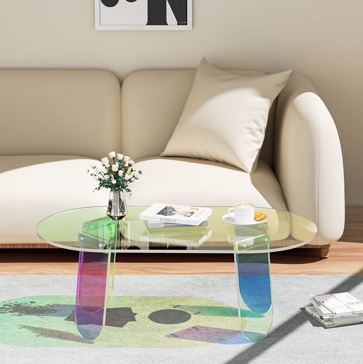 Transparent coffee table with books in a living room, featuring a rug and a beige sofa