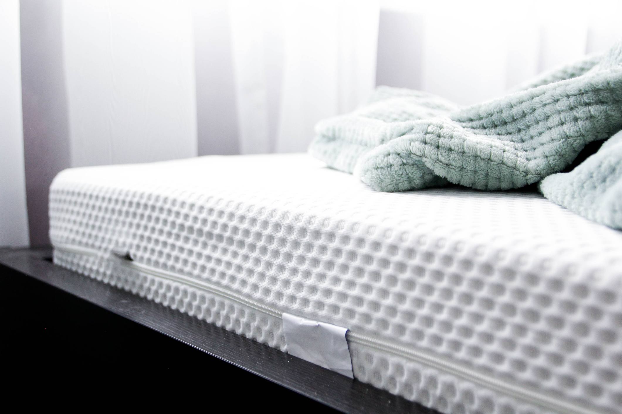 Close-up of a mattress corner with textured cover and a folded teal blanket