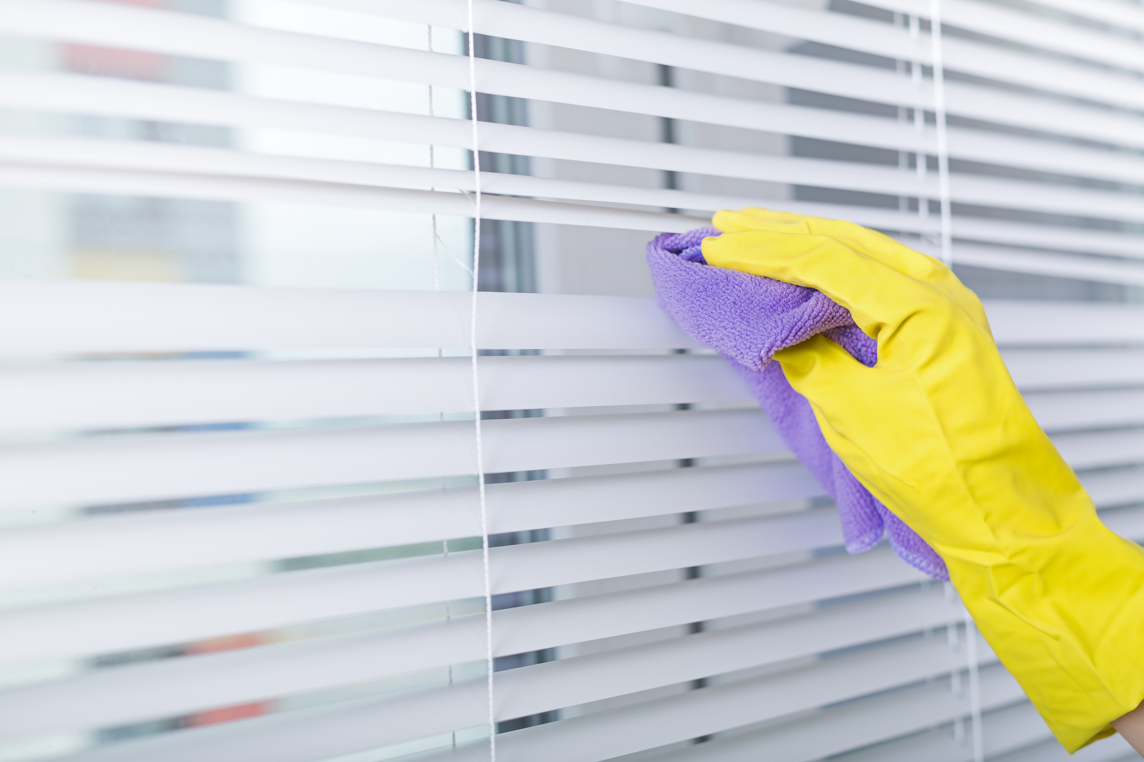 Hand in yellow glove dusting window blinds