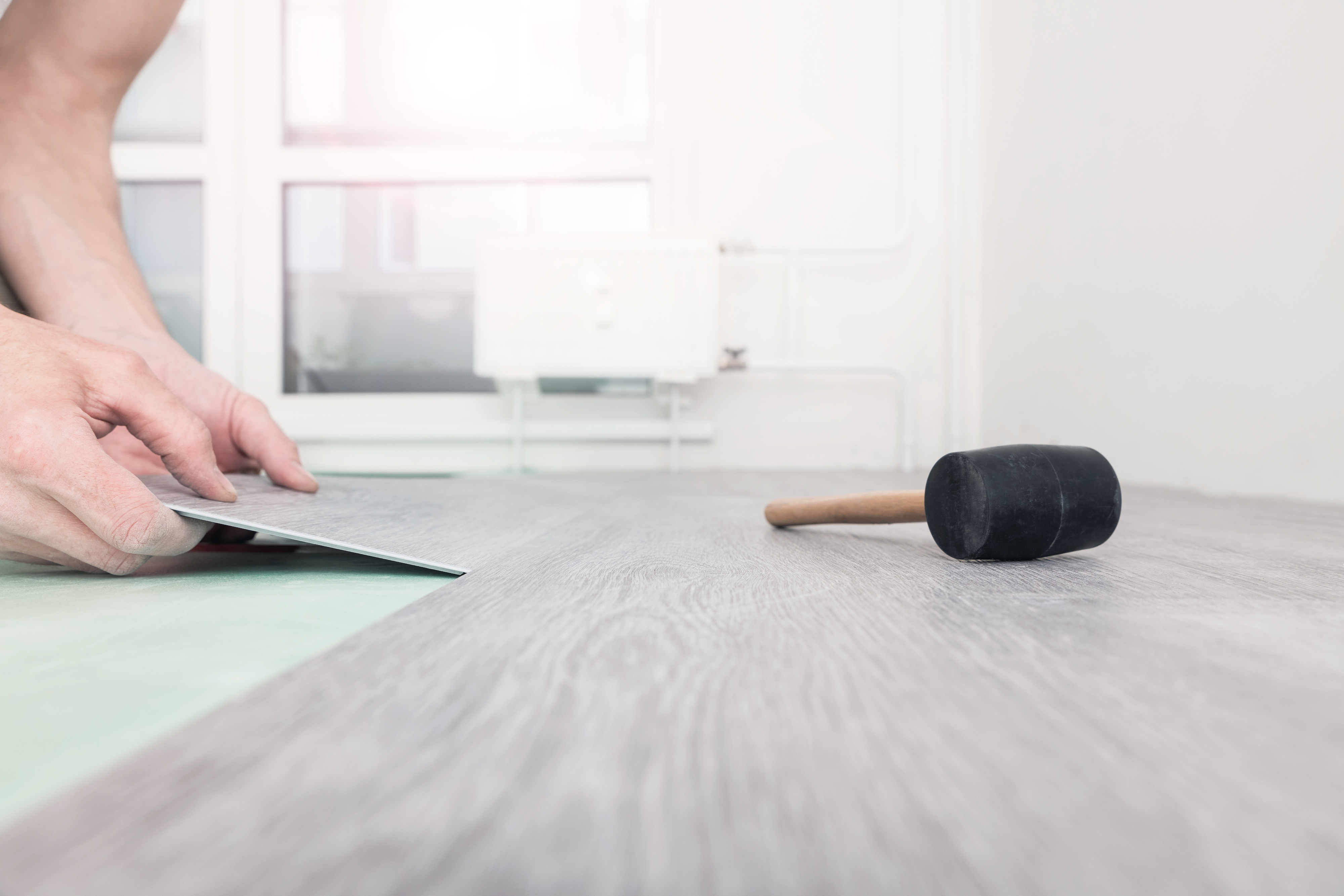 Hand installing new laminated wooden floor with a rubber mallet nearby