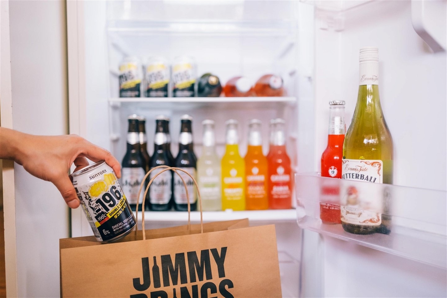 Hand reaching into a fridge taking a beverage near a paper bag with &#x27;JIMMY BRINGS&#x27; on it