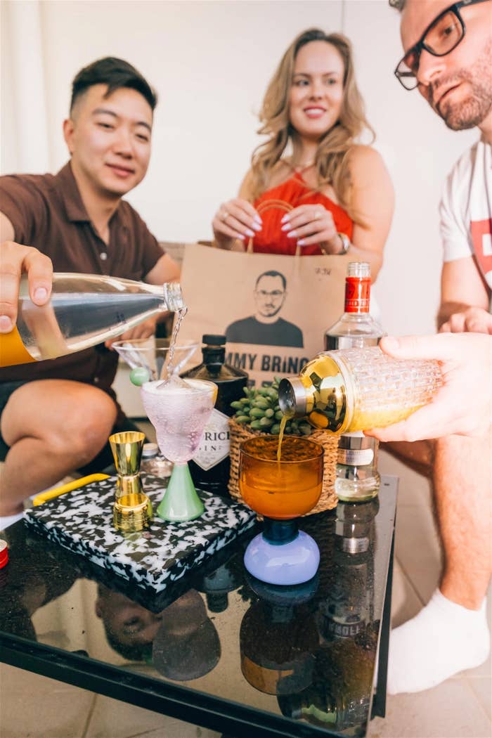 Three people having a casual gathering, pouring drinks, with a cocktail-making kit on the table