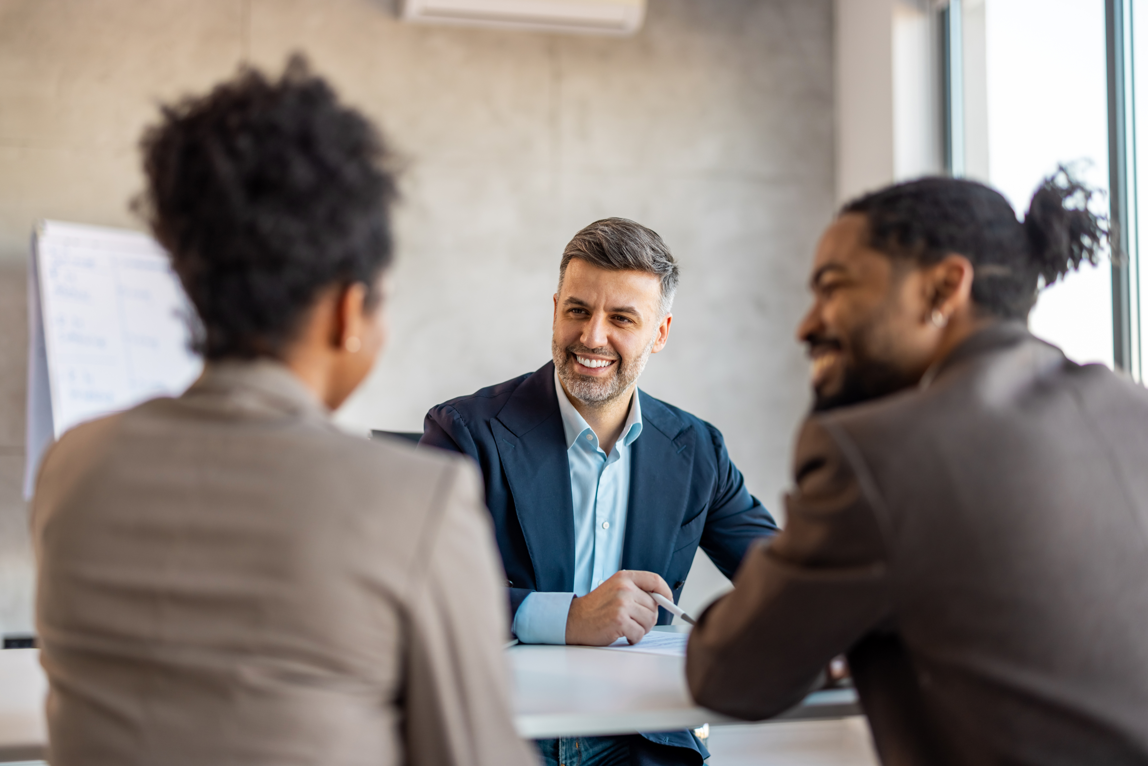 Three professionals in a meeting, one facing camera with a smile, others back to camera