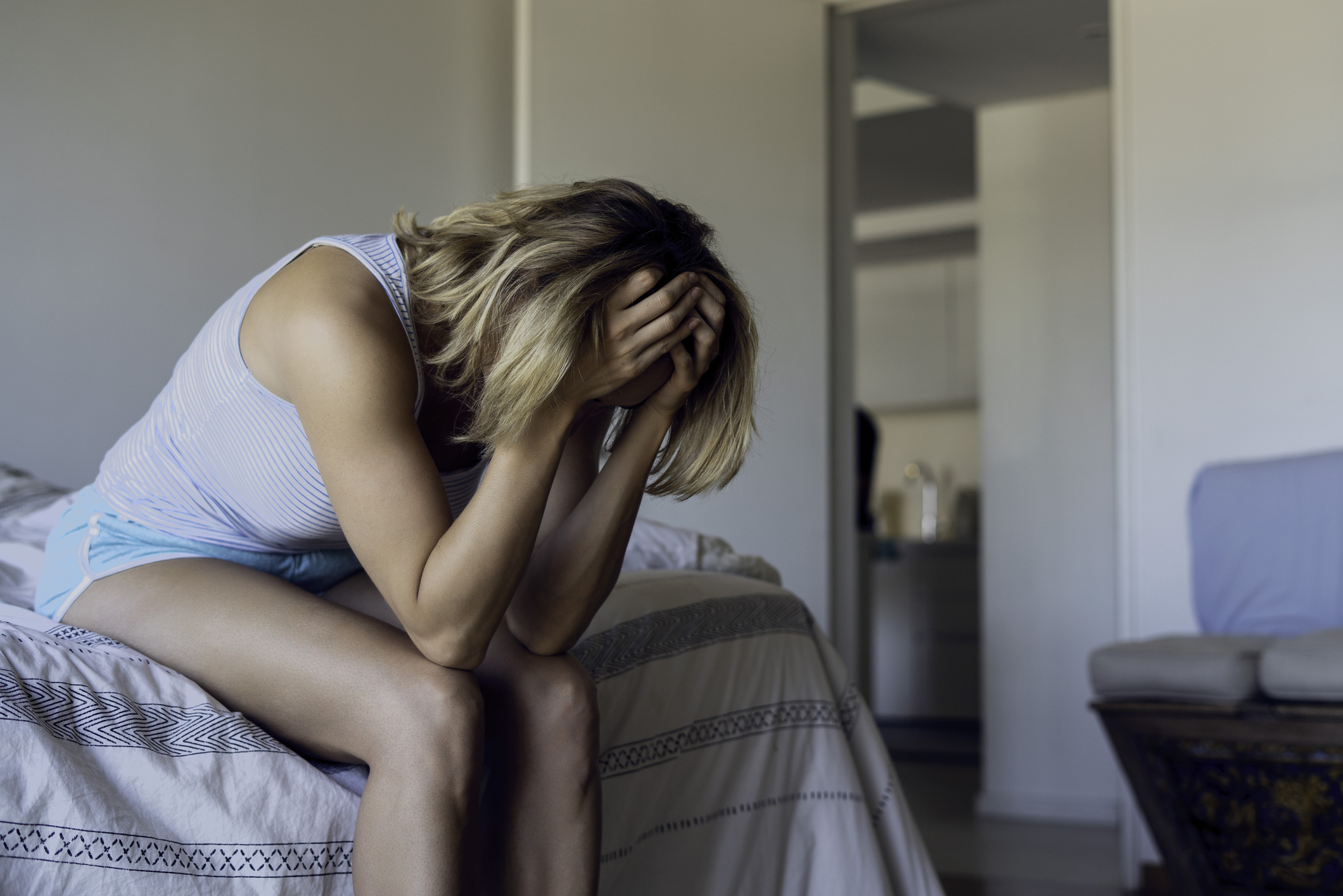 Person sitting on bed with head in hands, appearing distressed or upset