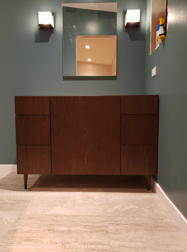 Wooden cabinet with doors in a room, mirror above, sconces on either side, no people