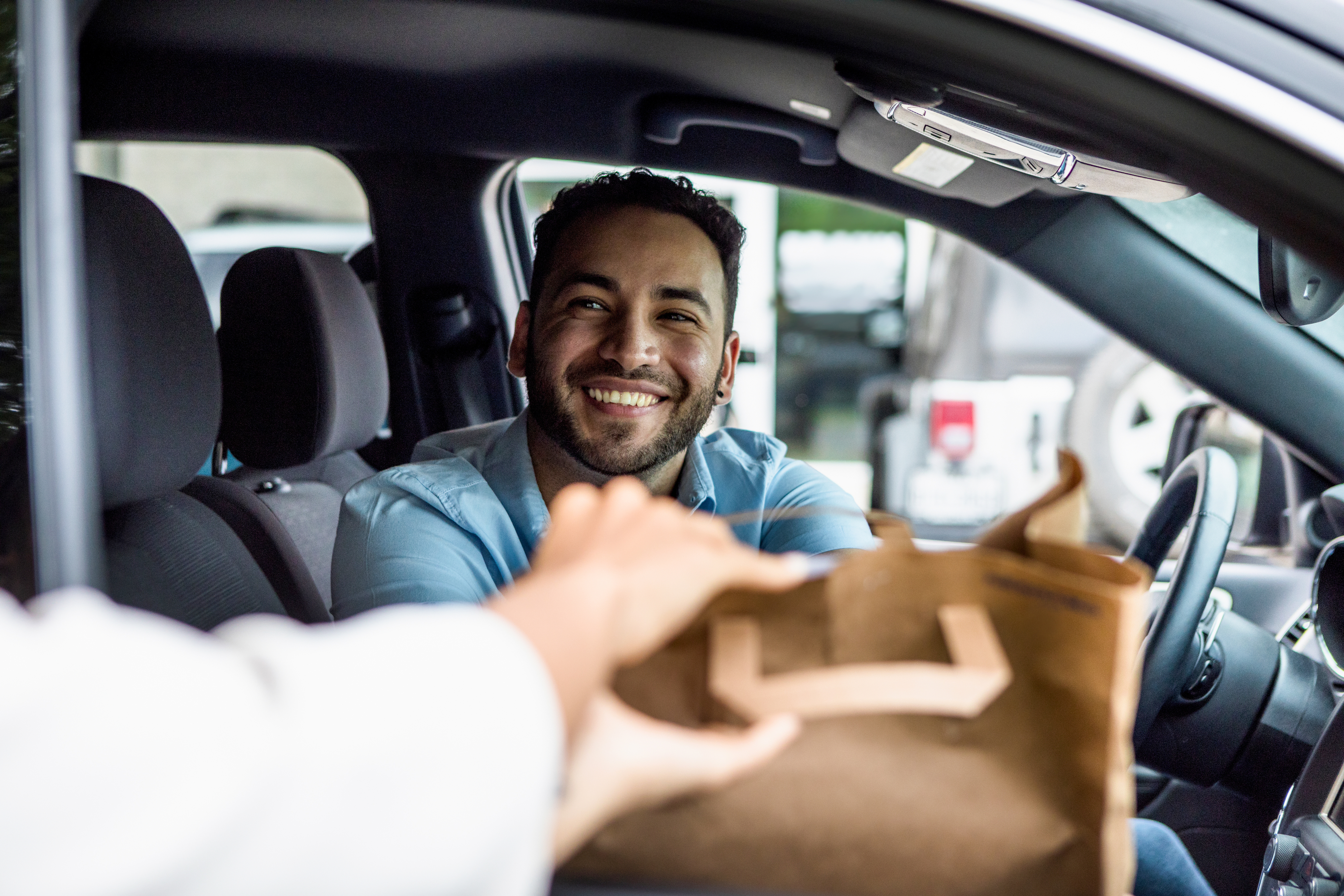 Person receiving a paper bag while sitting in a car, smiling at the camera