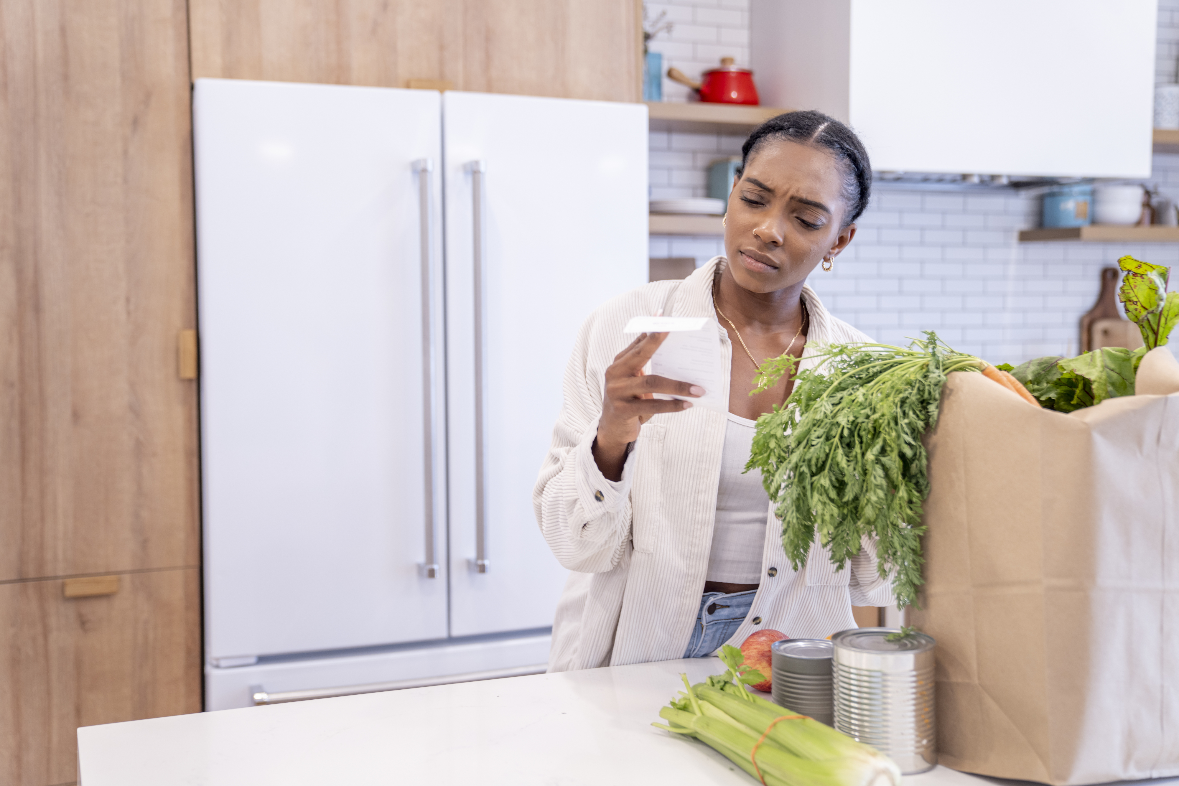 Woman checking grocery receipt, with fresh produce on counter