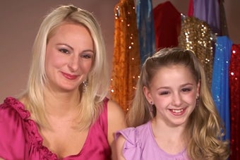 Woman and young girl smiling, seated, with sparkly dresses in background