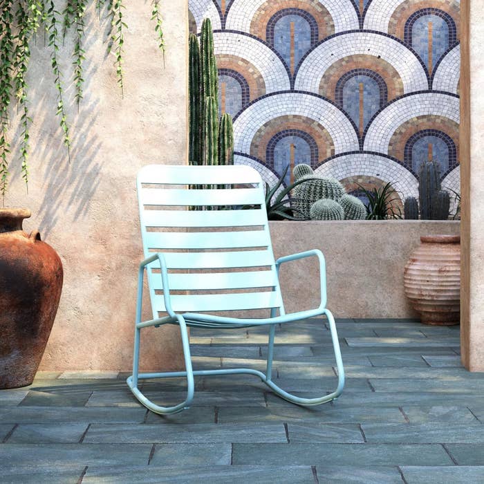 Modern metal outdoor chair on a patio surrounded by plants and mosaic wall art