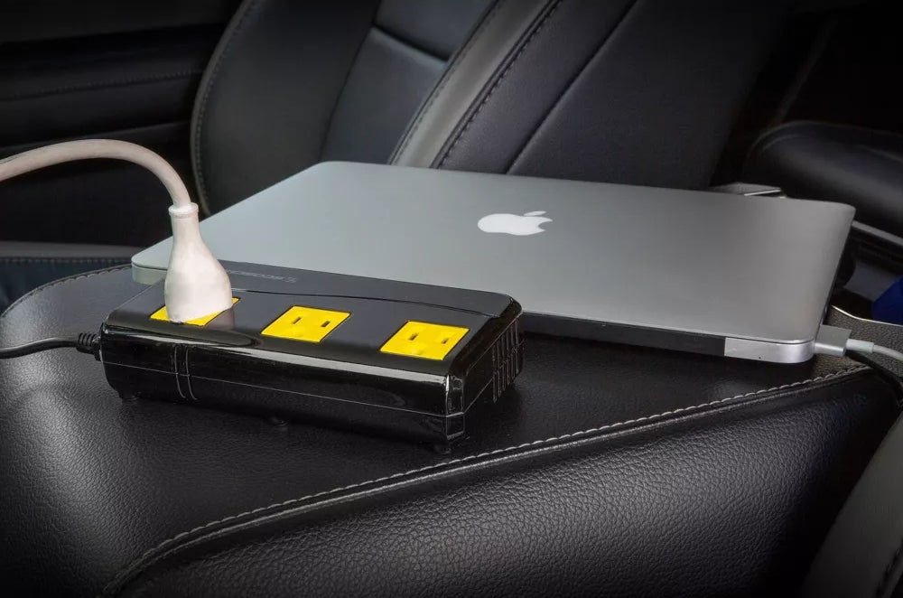 Laptop charging through a portable car charger on a seat, useful for on-the-go power needs
