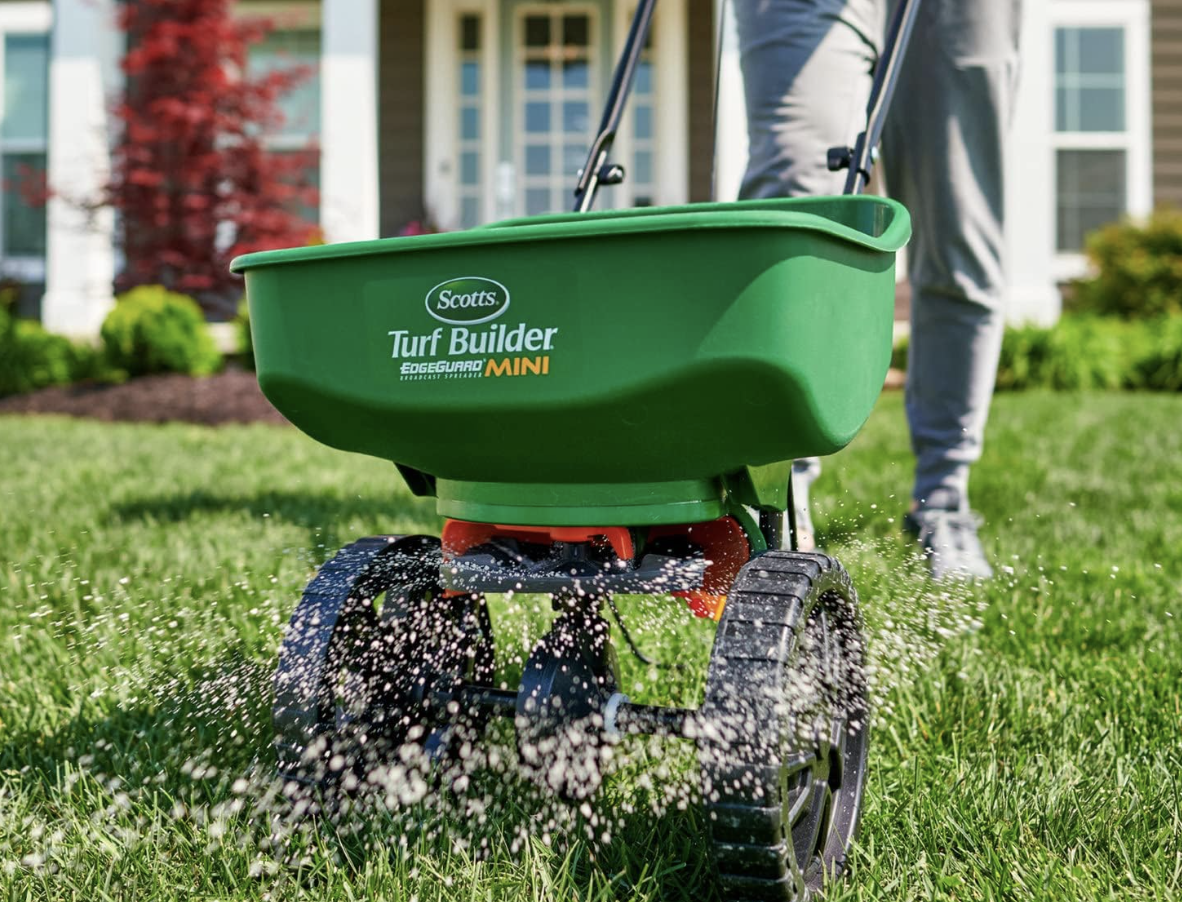 A model using a Scotts Turf Builder Mini spreader on a lawn