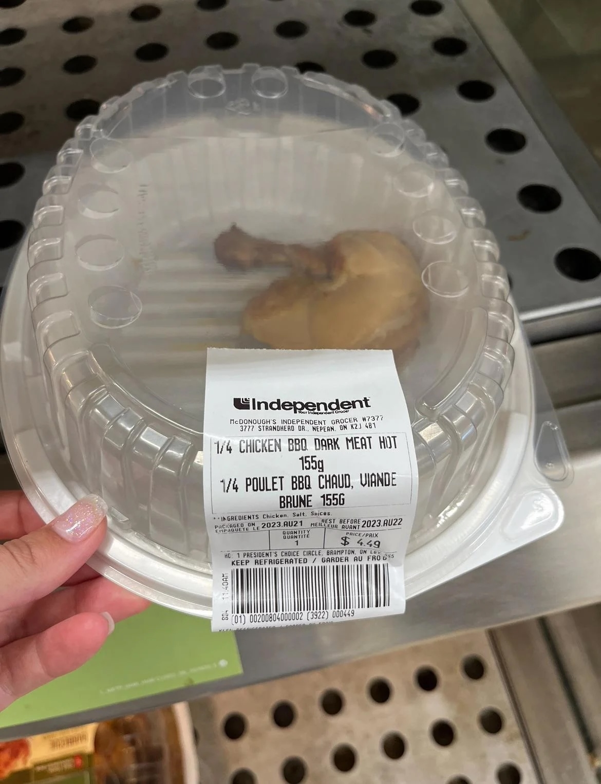 Hand holding a clear plastic container with a partial rotisserie chicken and a label showing product details and pricing