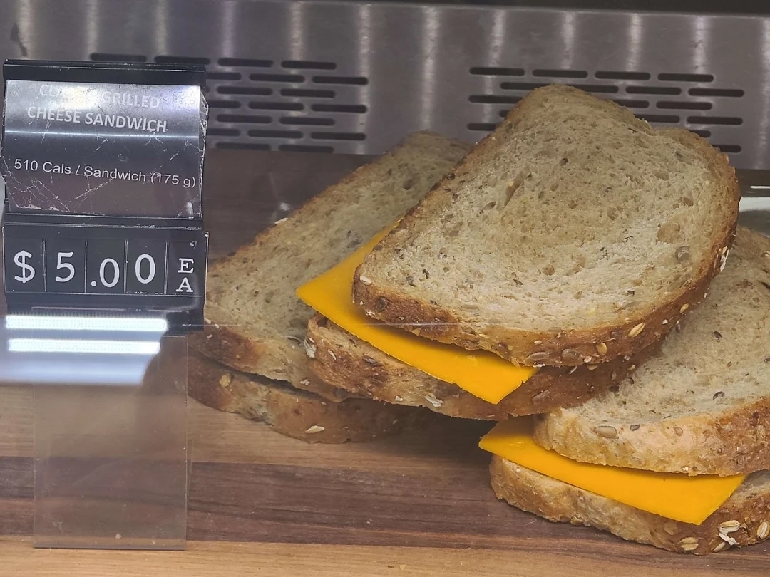 Grilled cheese sandwich with a visible slice of cheese, priced at $5.00, displayed behind a label stating calories and price