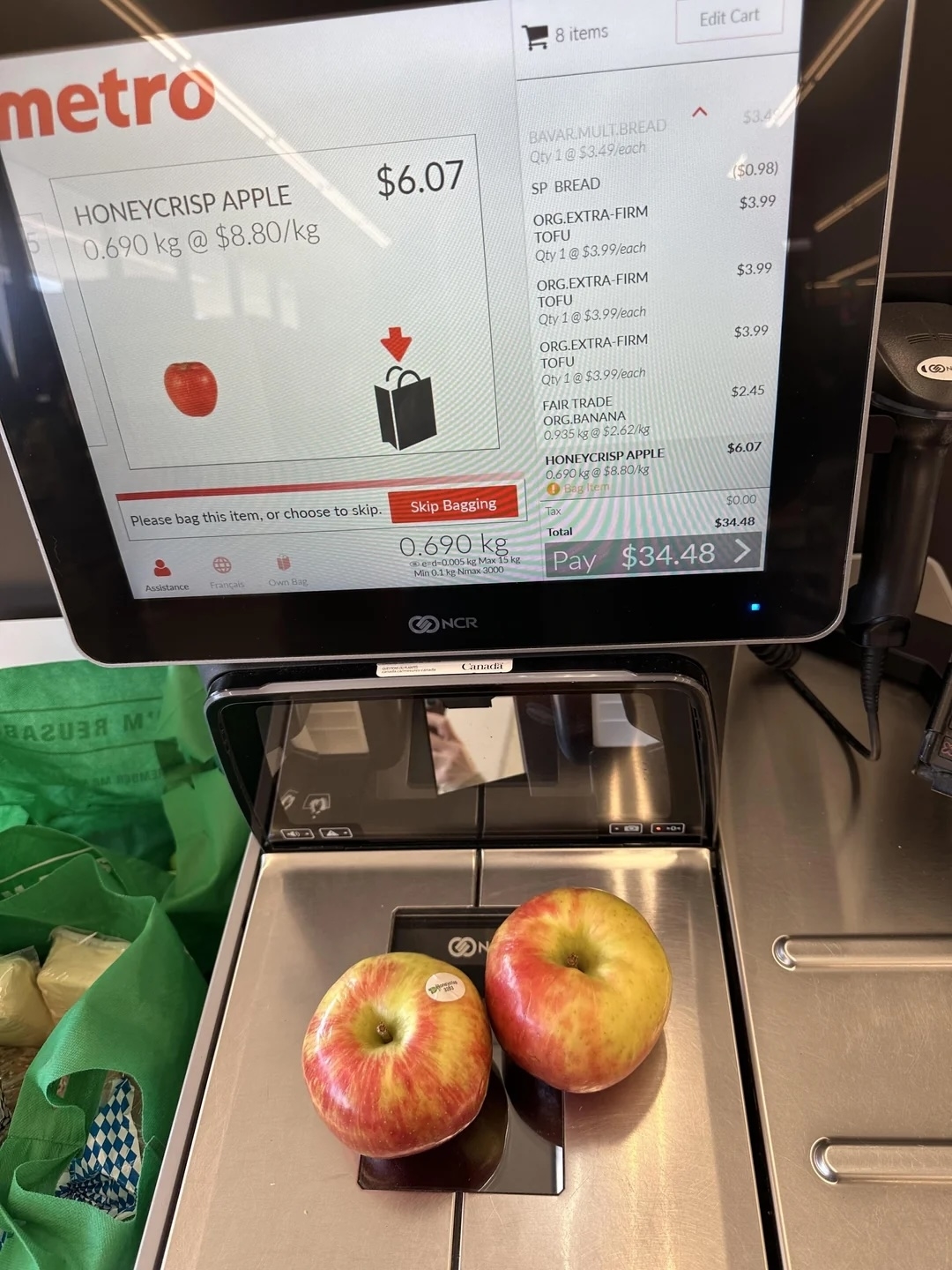 Two apples on a grocery scale with a checkout screen displaying a total of $6.07 in a self-service kiosk
