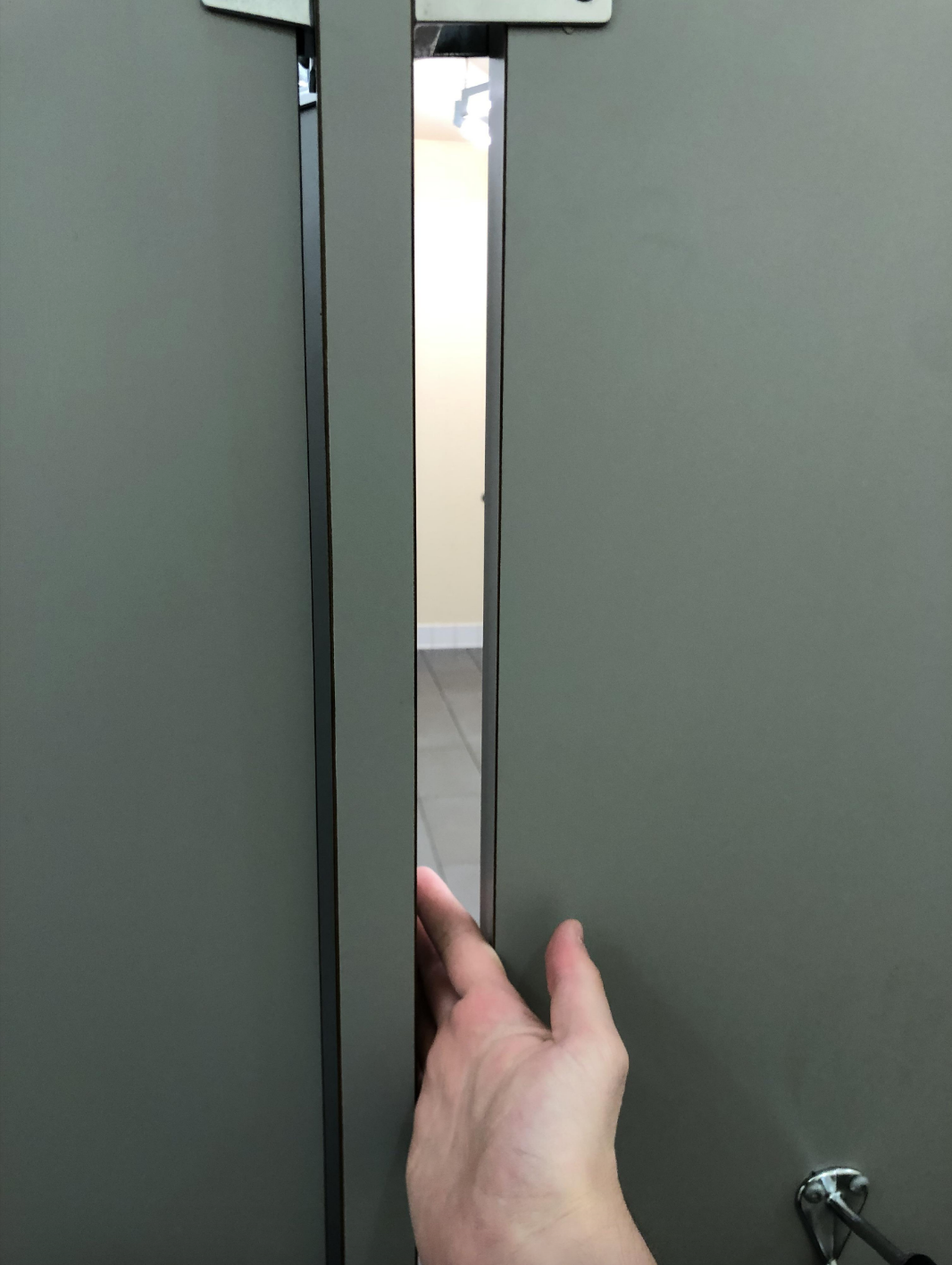 Person&#x27;s hand pushing a stall door slightly ajar in a restroom, highlighting a privacy concern