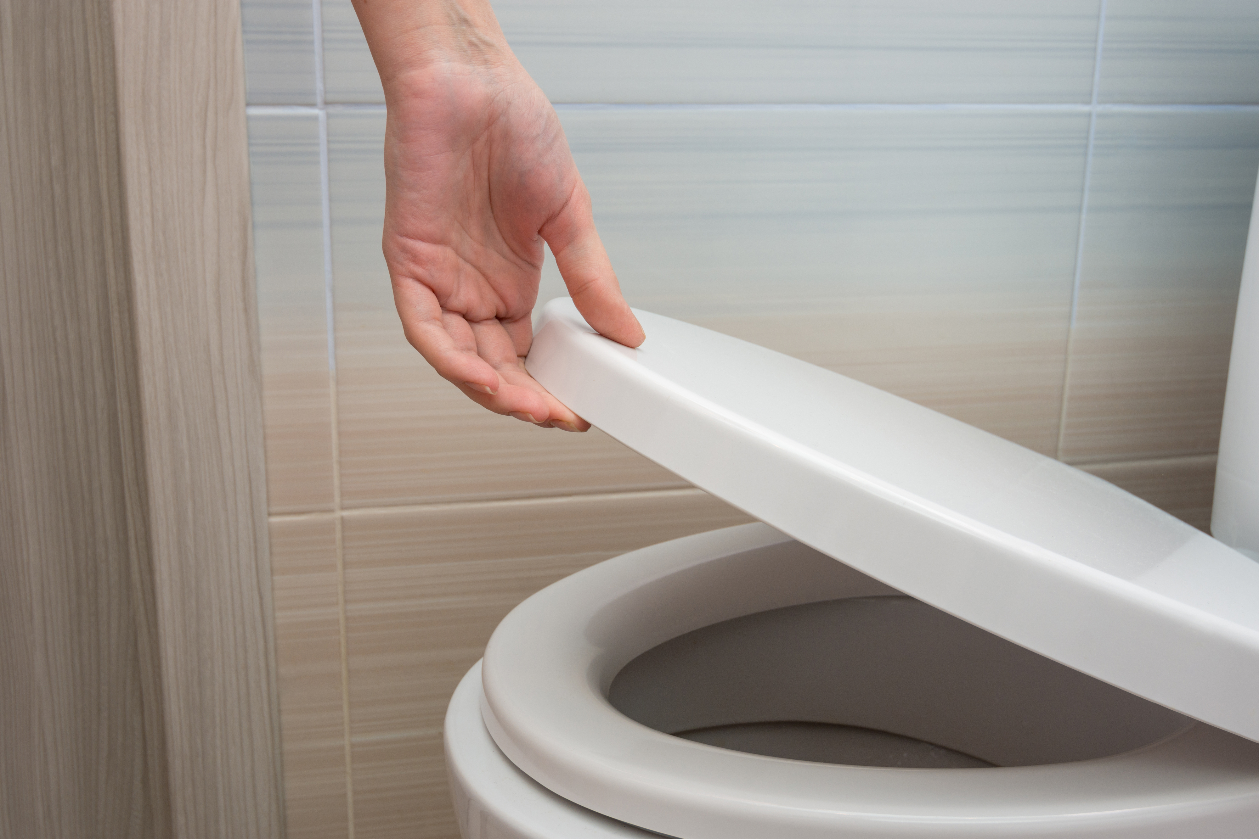 Person raising a white toilet seat in a bathroom