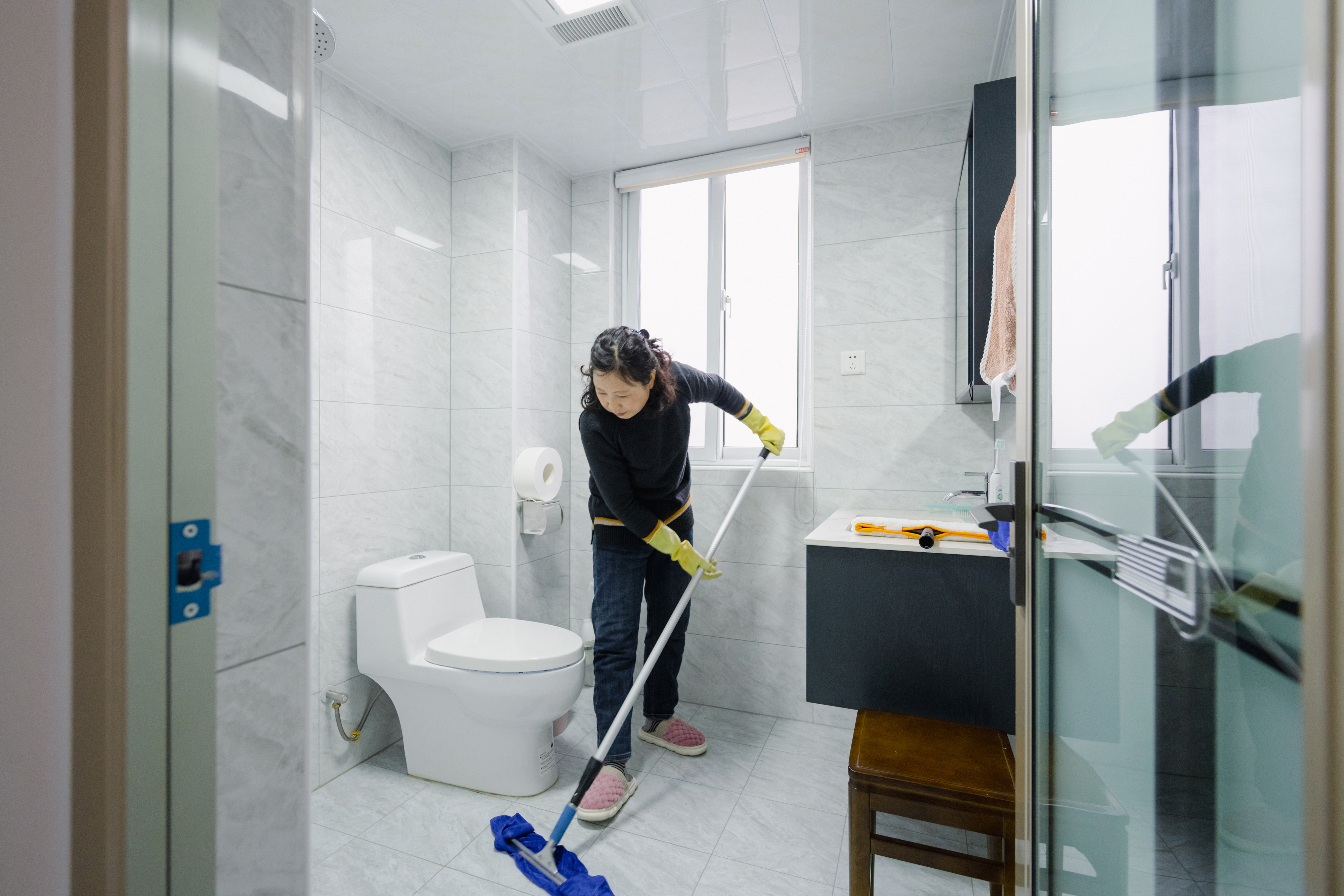 Person mopping floor in a bathroom with cleaning supplies nearby