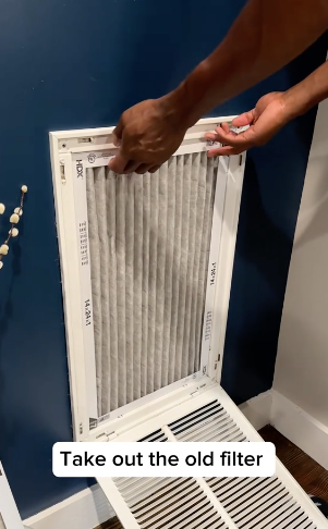 Person replacing an air filter in a wall vent, with text &quot;Take out the old filter&quot;