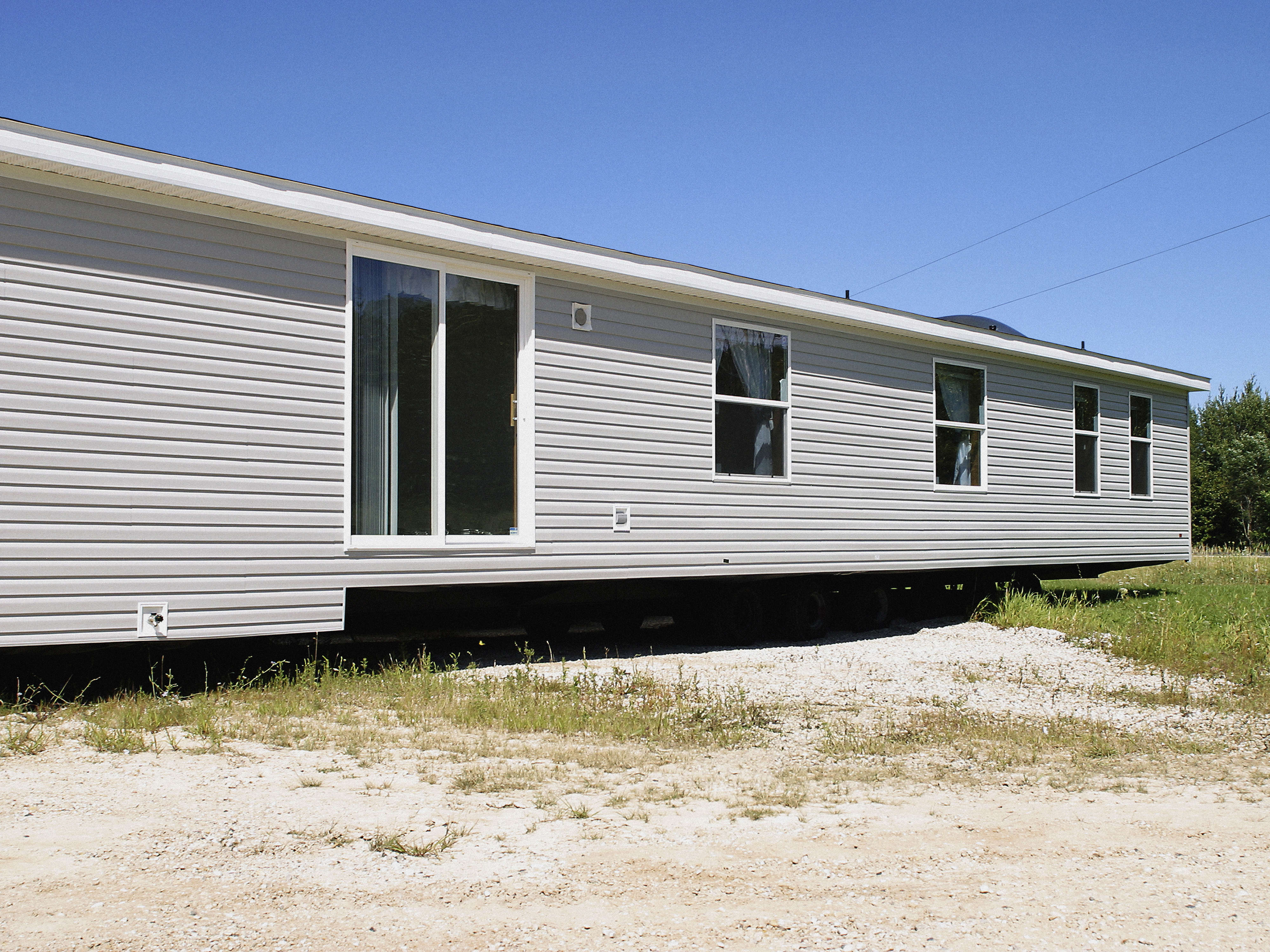 Modular home on a temporary foundation with visible undercarriage, placed in a clear, grassy area