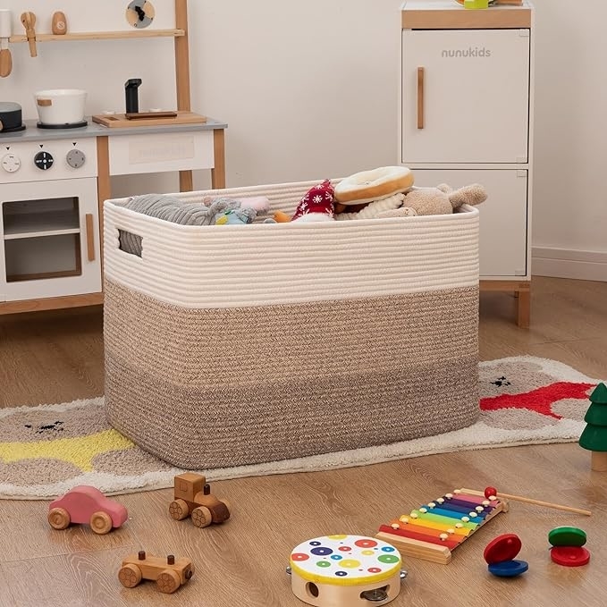 A cozy playroom with toys including a large woven storage basket packed with stuffed animals, wooden cars, a xylophone, and a toy kitchen in the background