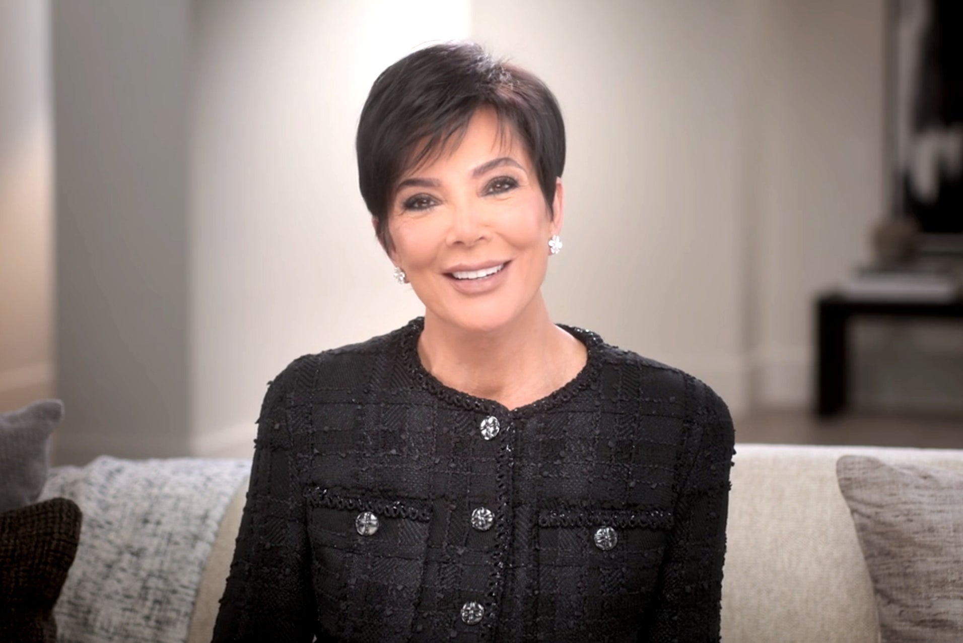 Kris Jenner smiles while sitting on a couch