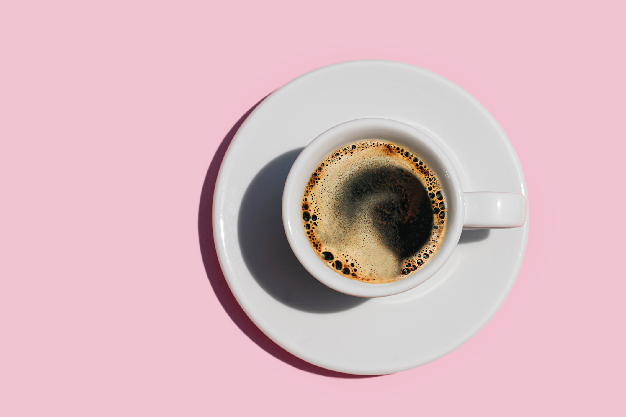 A cup of black coffee sits on a white saucer against a plain background
