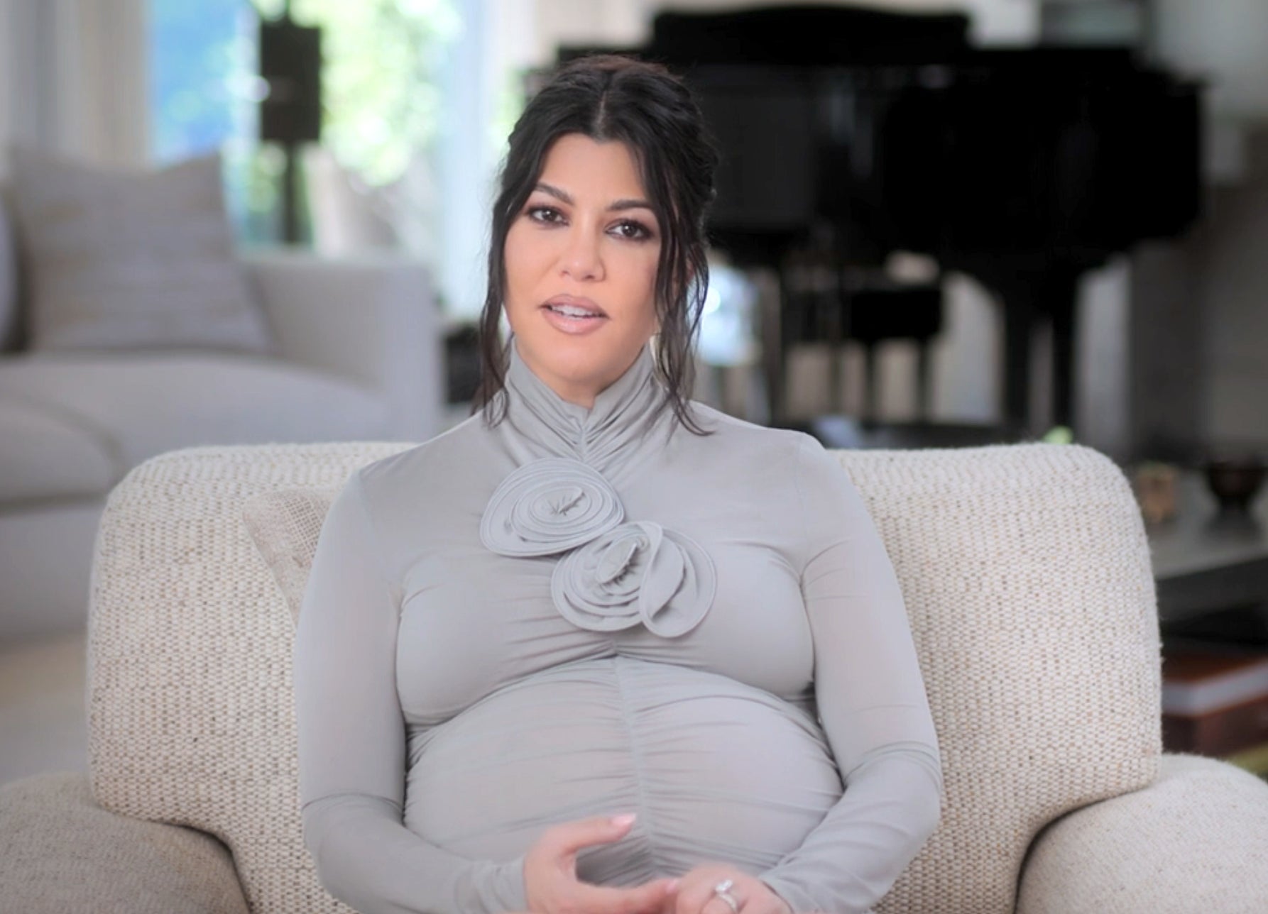 A pregnant Kourtney Kardashian sits on a couch in a living room setting