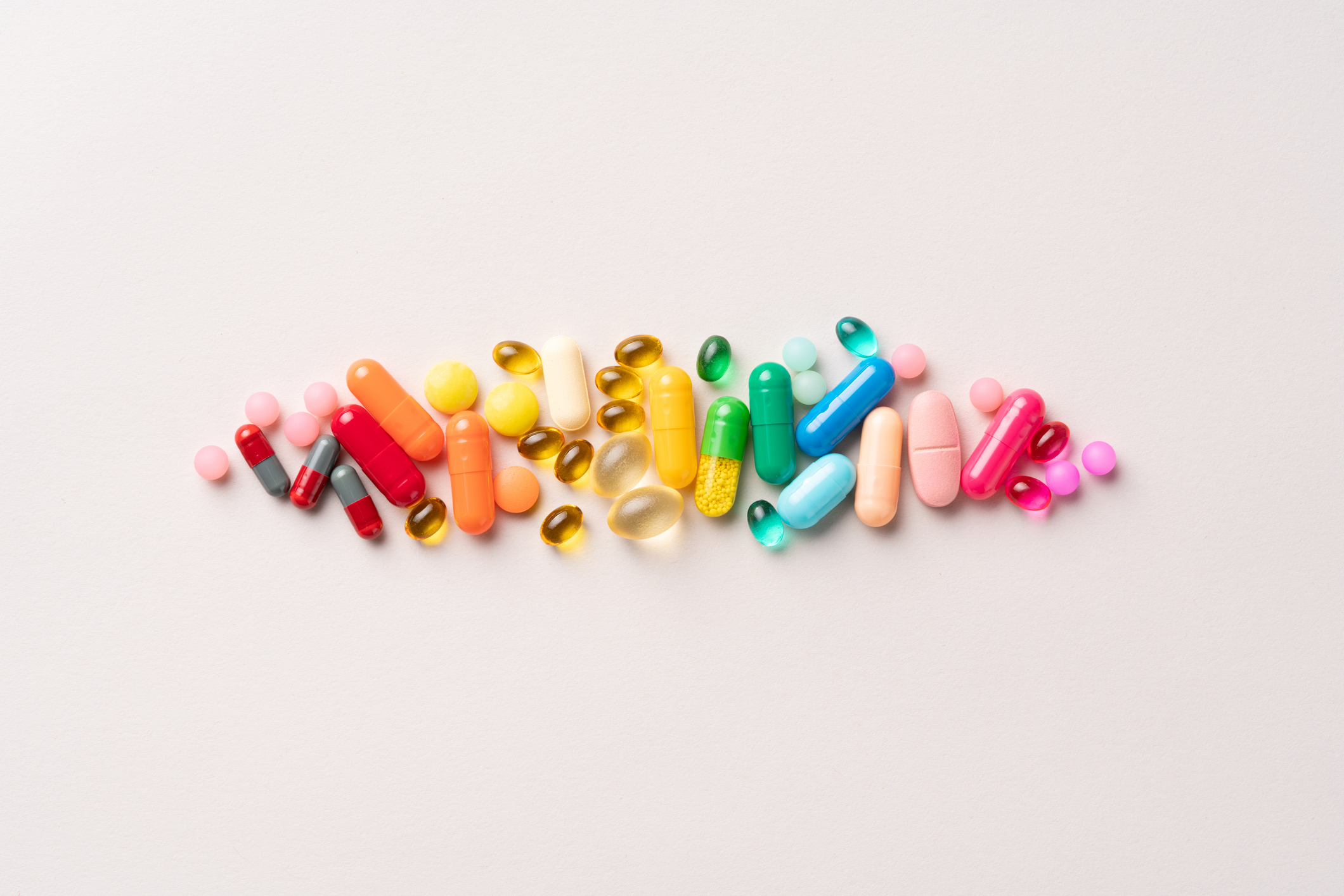 A variety of pills and capsules of different shapes and sizes are arranged in a row on a plain background, depicting various types of medication