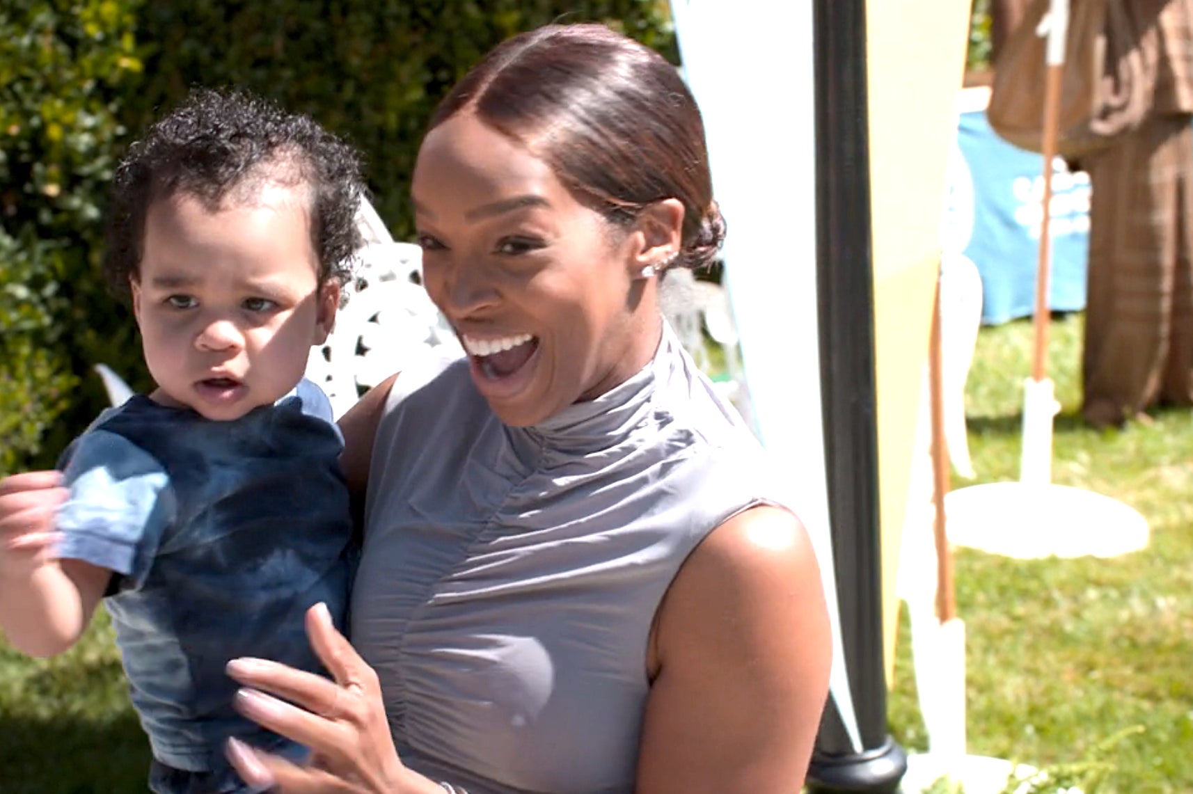 Malika smiles while holding Tatum at an outdoor event