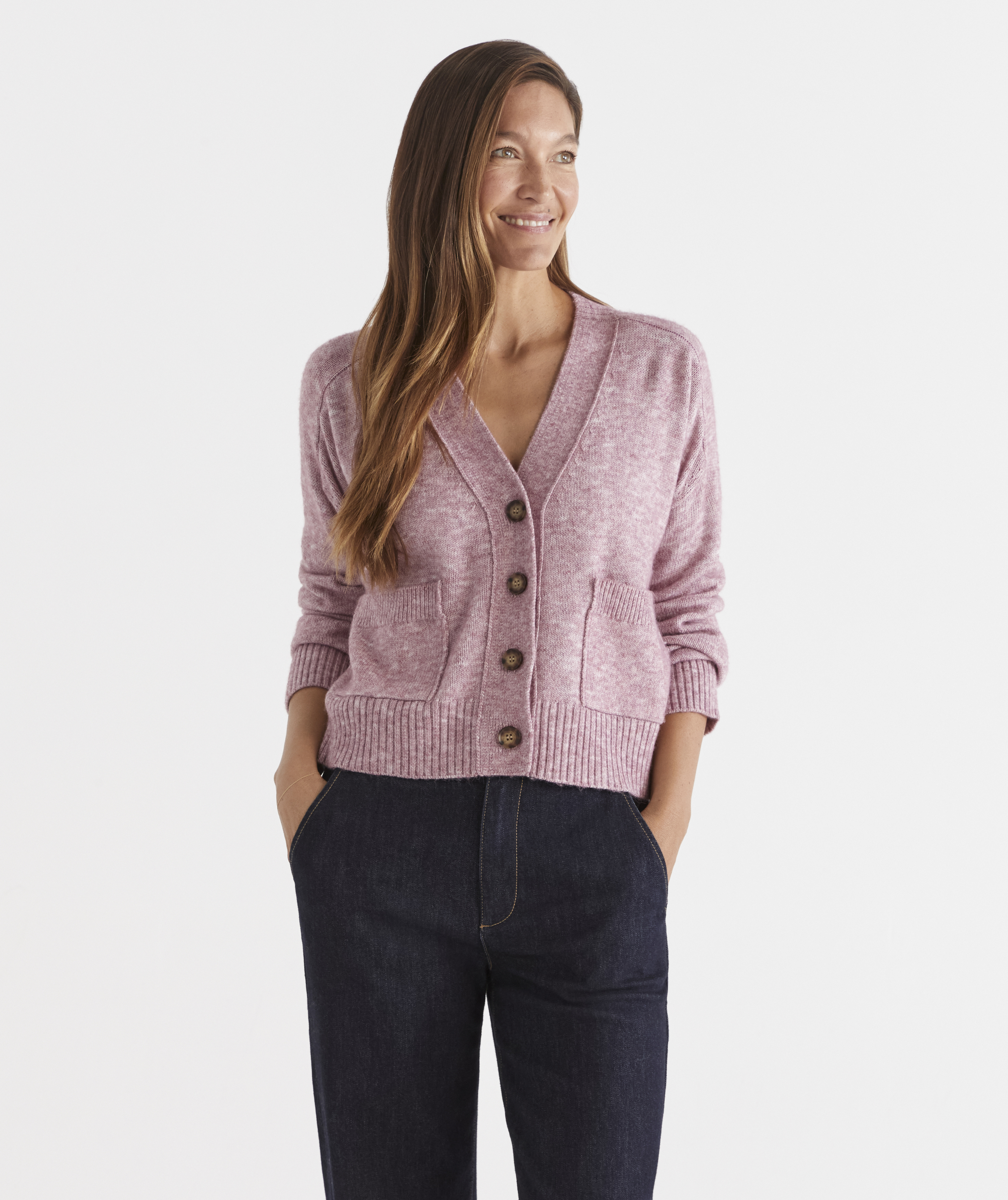 A woman is smiling and wearing a cozy, button-up cardigan with pockets, paired with dark pants