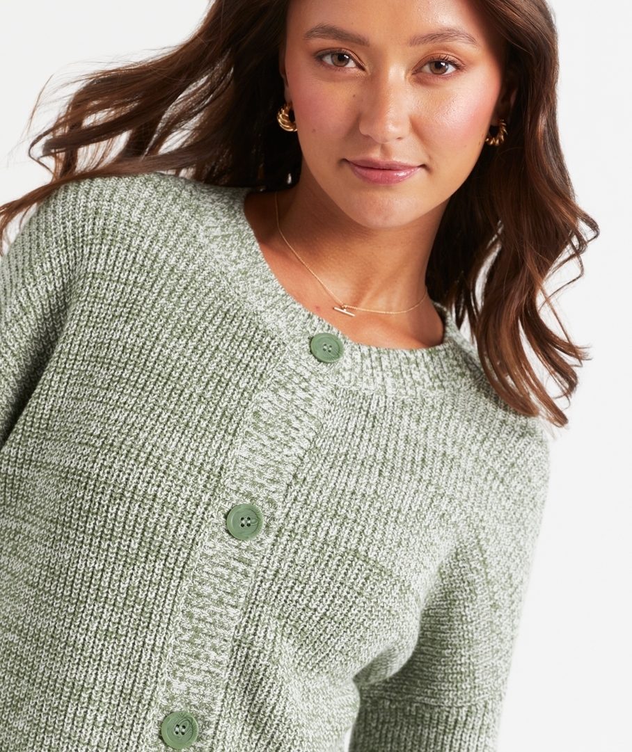Woman poses in a cozy knit cardigan with large buttons, showcasing a stylish outfit for a shopping article