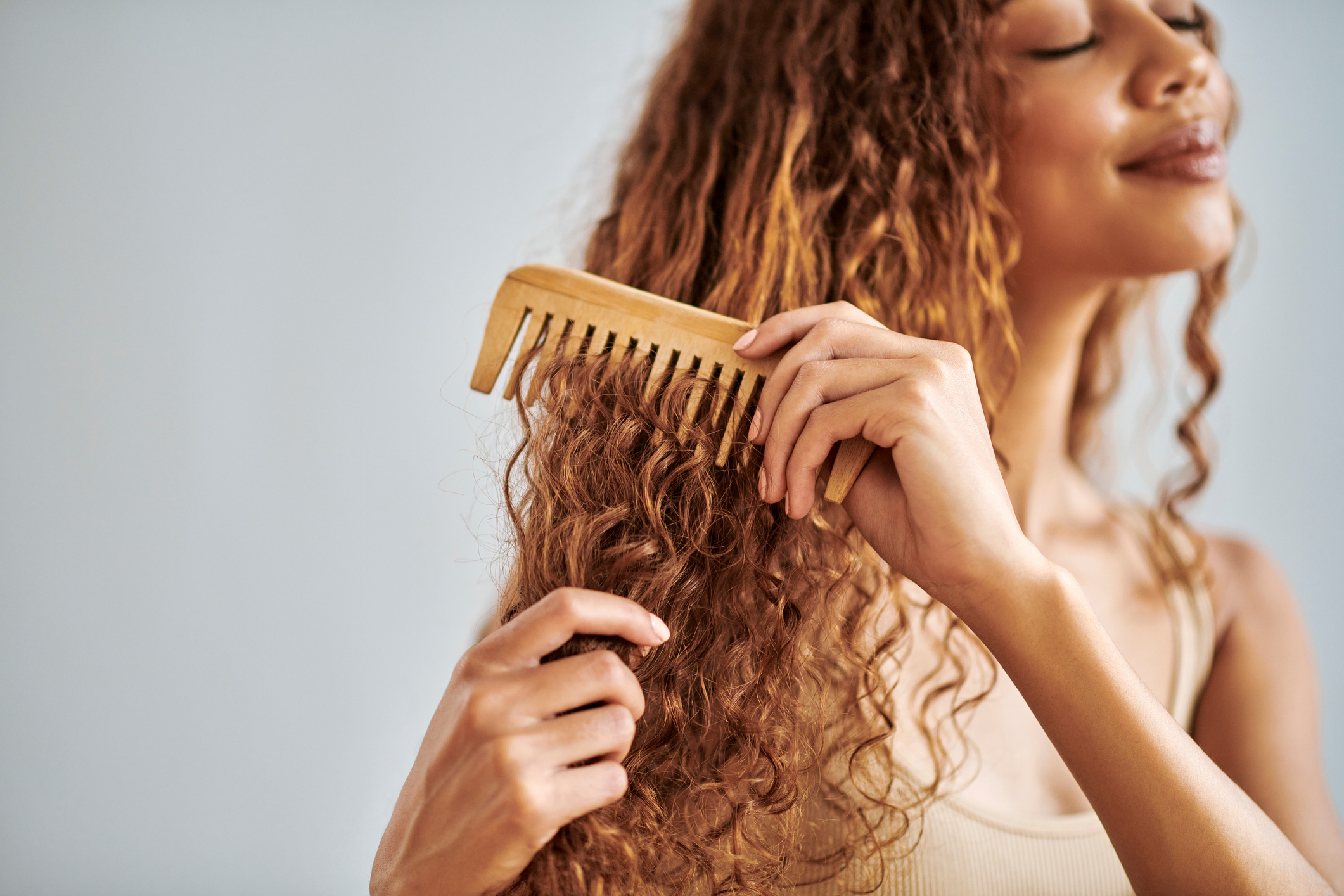 Woman combs her curly hair with a wooden comb, smiling with eyes closed in a serene moment