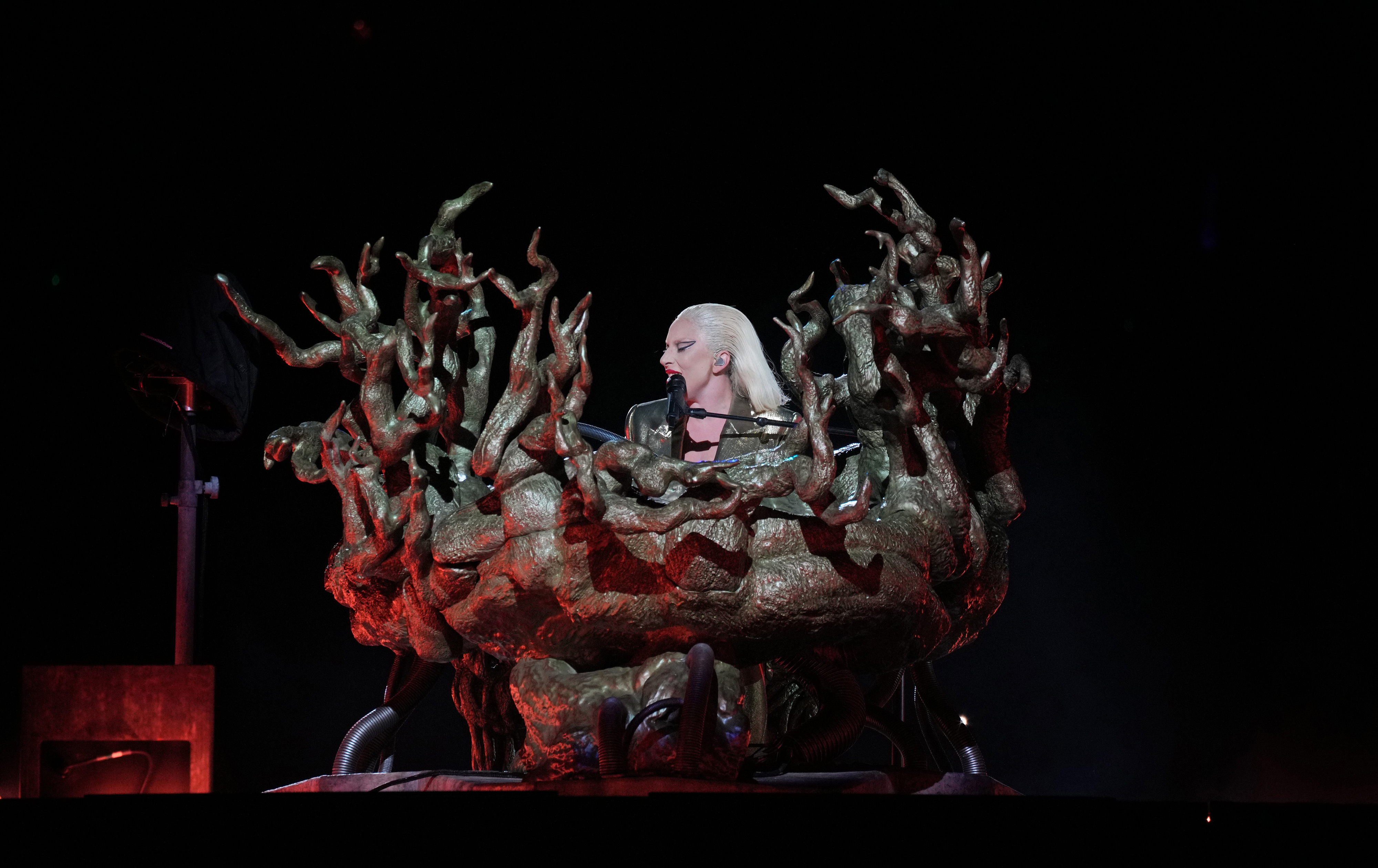 Lady Gaga performing on stage, seated in an elaborate, artistically designed structure resembling twisted branches