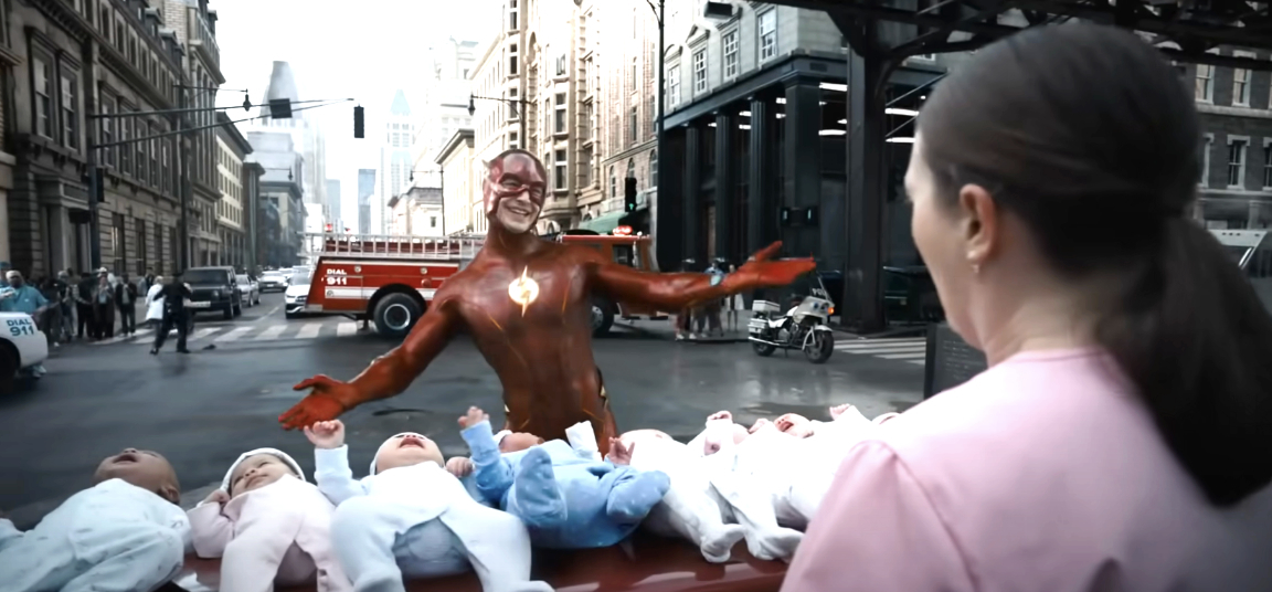 The Flash (Ezra Miller) standing in the street, smiling, surrounded by several babies in a city setting, with a woman looking on