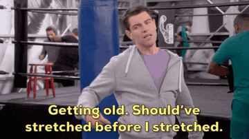 Max Greenfield in a gym, rubbing his back and saying, &quot;Getting old. Should&#x27;ve stretched before I stretched.&quot; People are working out in the background