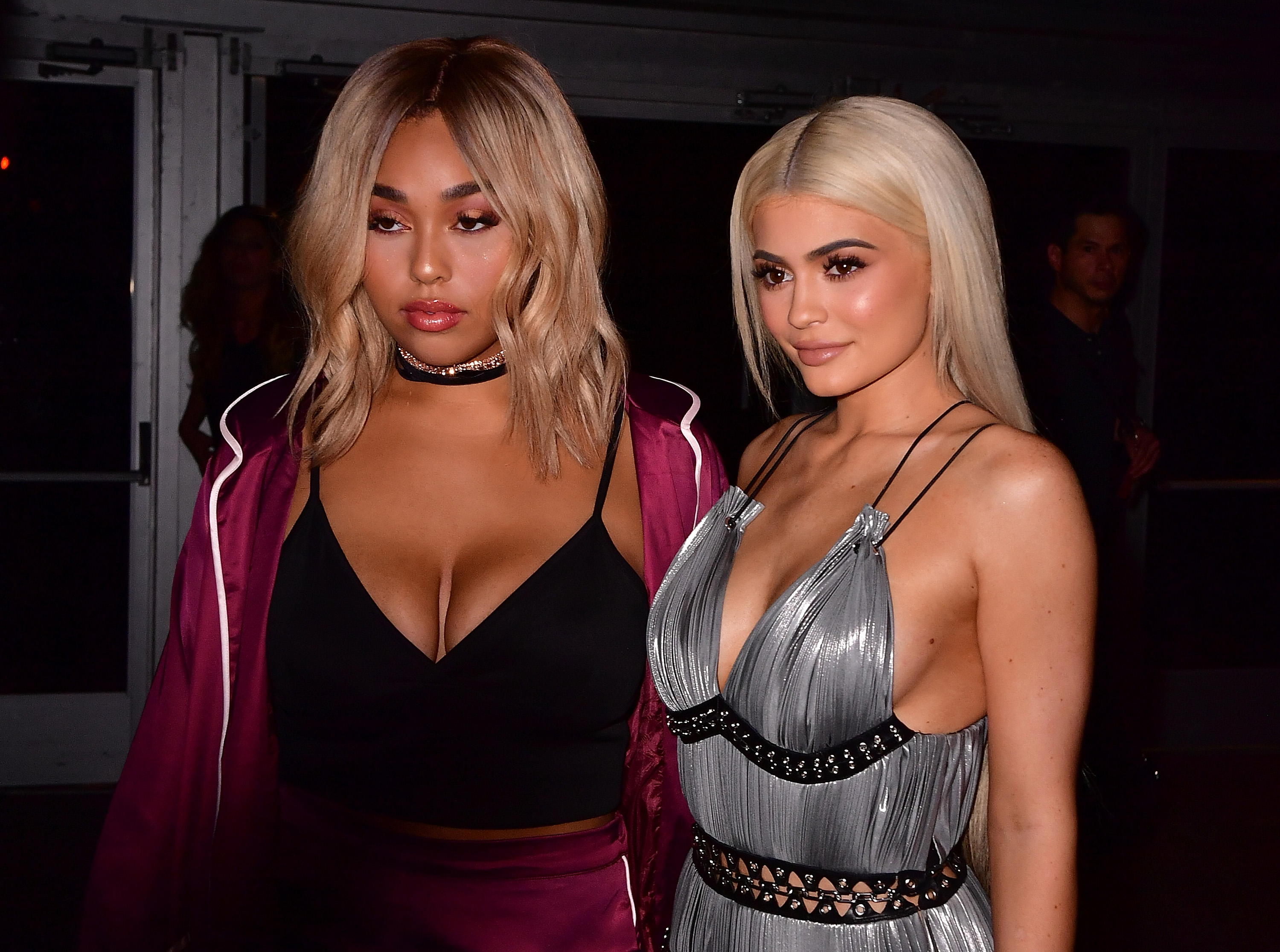 Jordyn Woods wearing a black top with a maroon jacket and Kylie Jenner in a silver fringe dress at an event