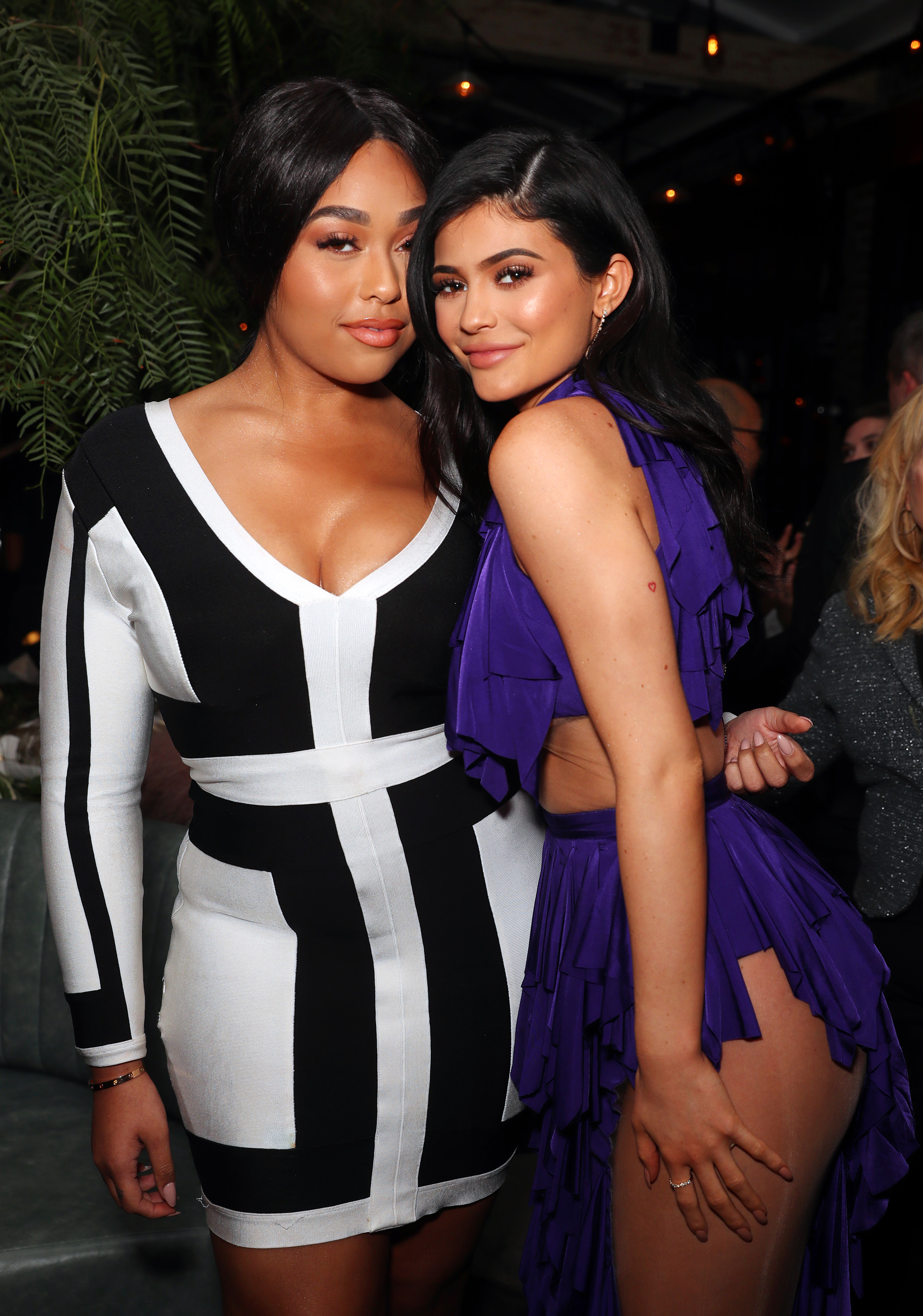 Jordyn Woods and Kylie Jenner posing together indoors, with Jordyn in a black and white dress and Kylie in a purple dress