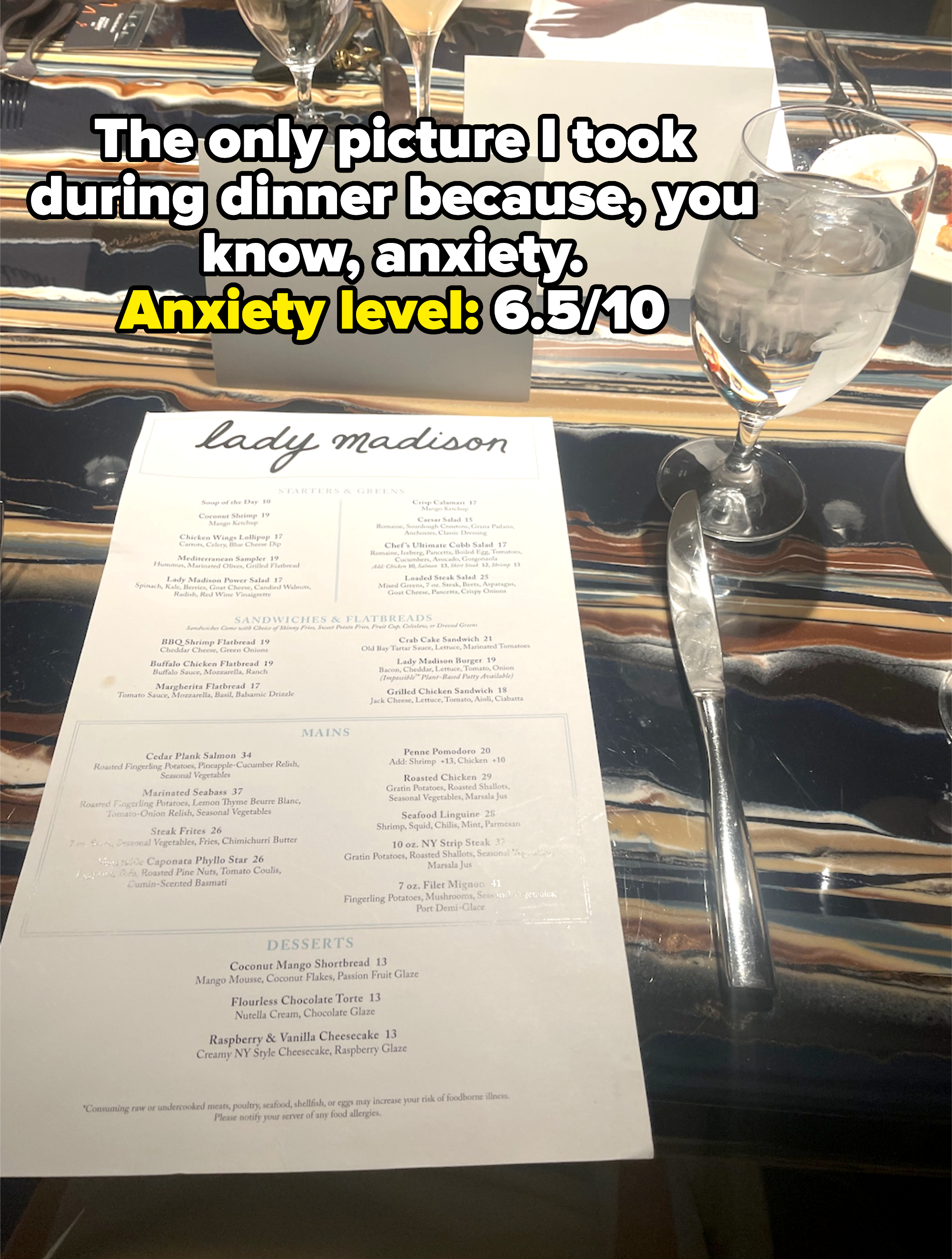 A dinner menu from a restaurant named Lady Madison is shown on a table set with a water glass, fork, knife, and a name card