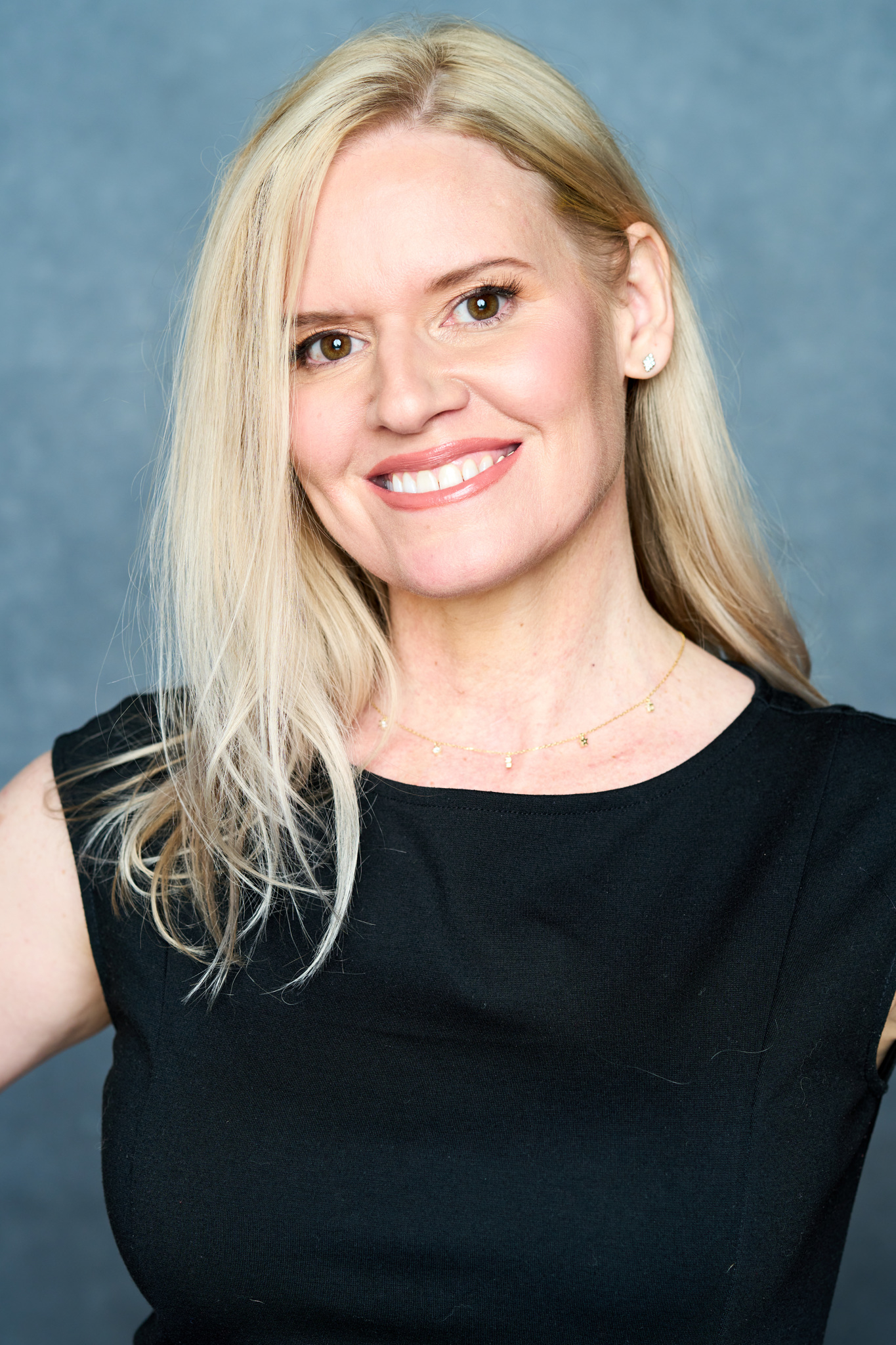 Smiling woman with shoulder-length blonde hair wearing a sleeveless black top against a plain background