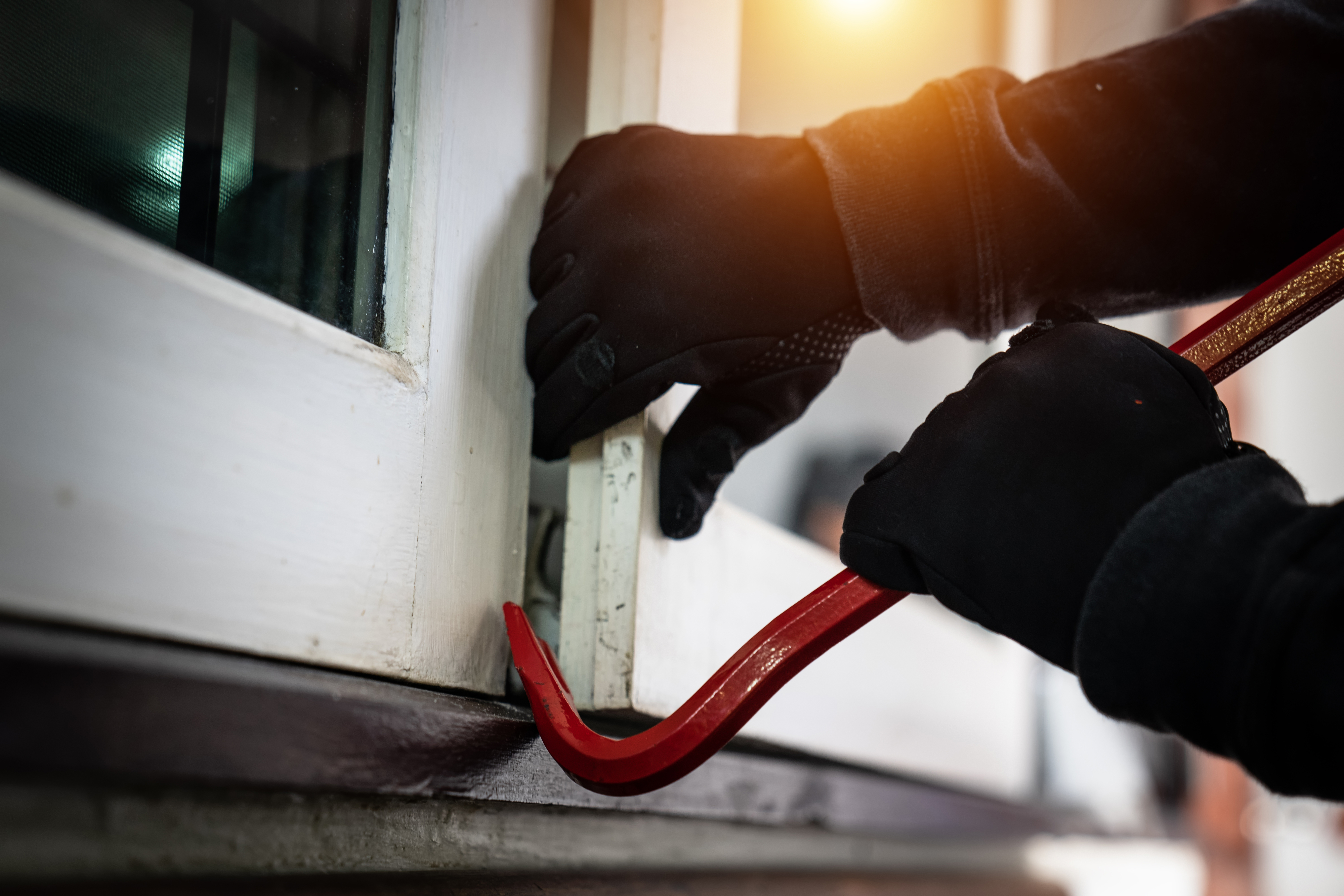 Gloved hands using a crowbar to pry open a window