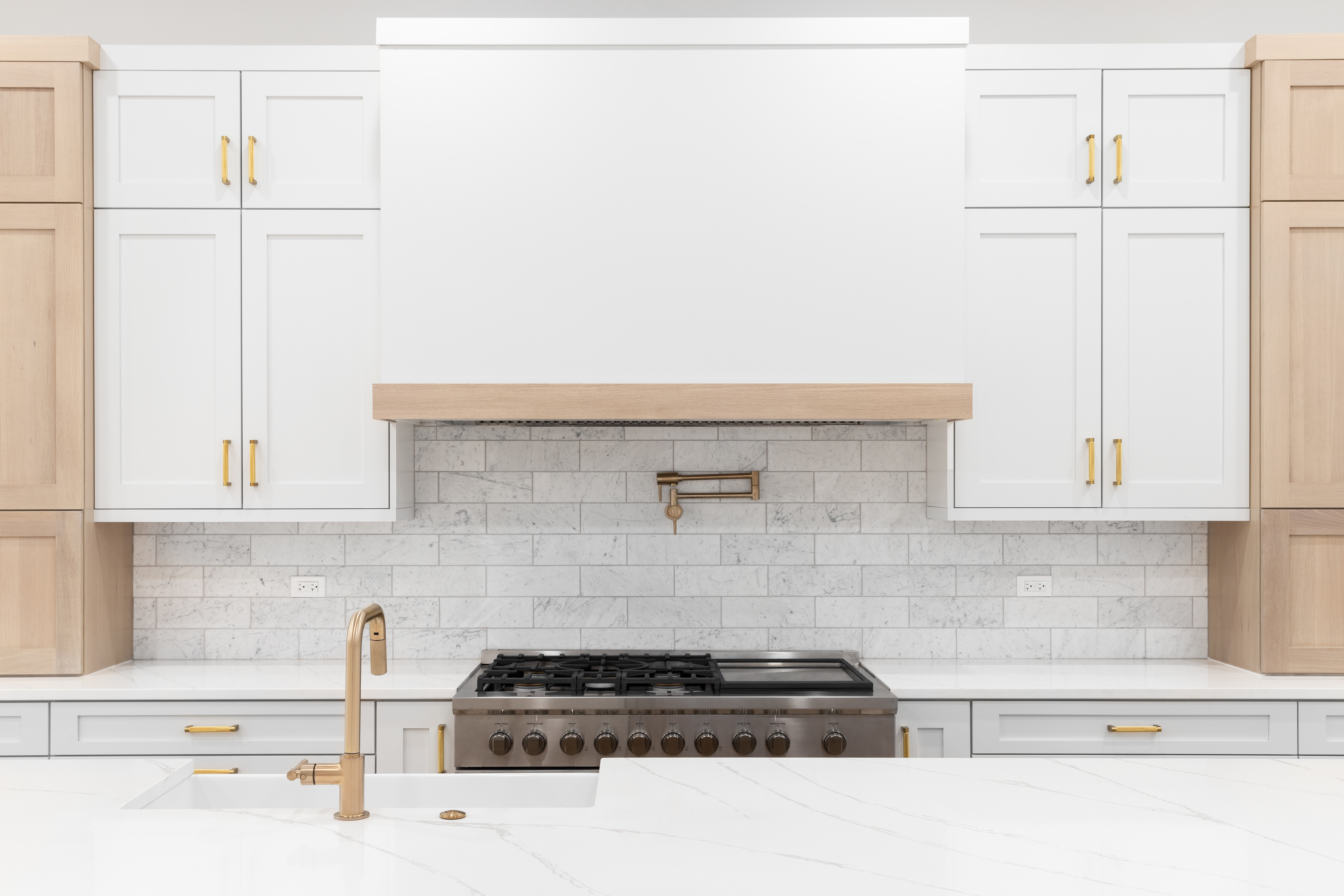 Modern kitchen with white cabinets, marble countertops, a stainless steel oven, and a gold faucet with a pot filler above the stove. No persons visible