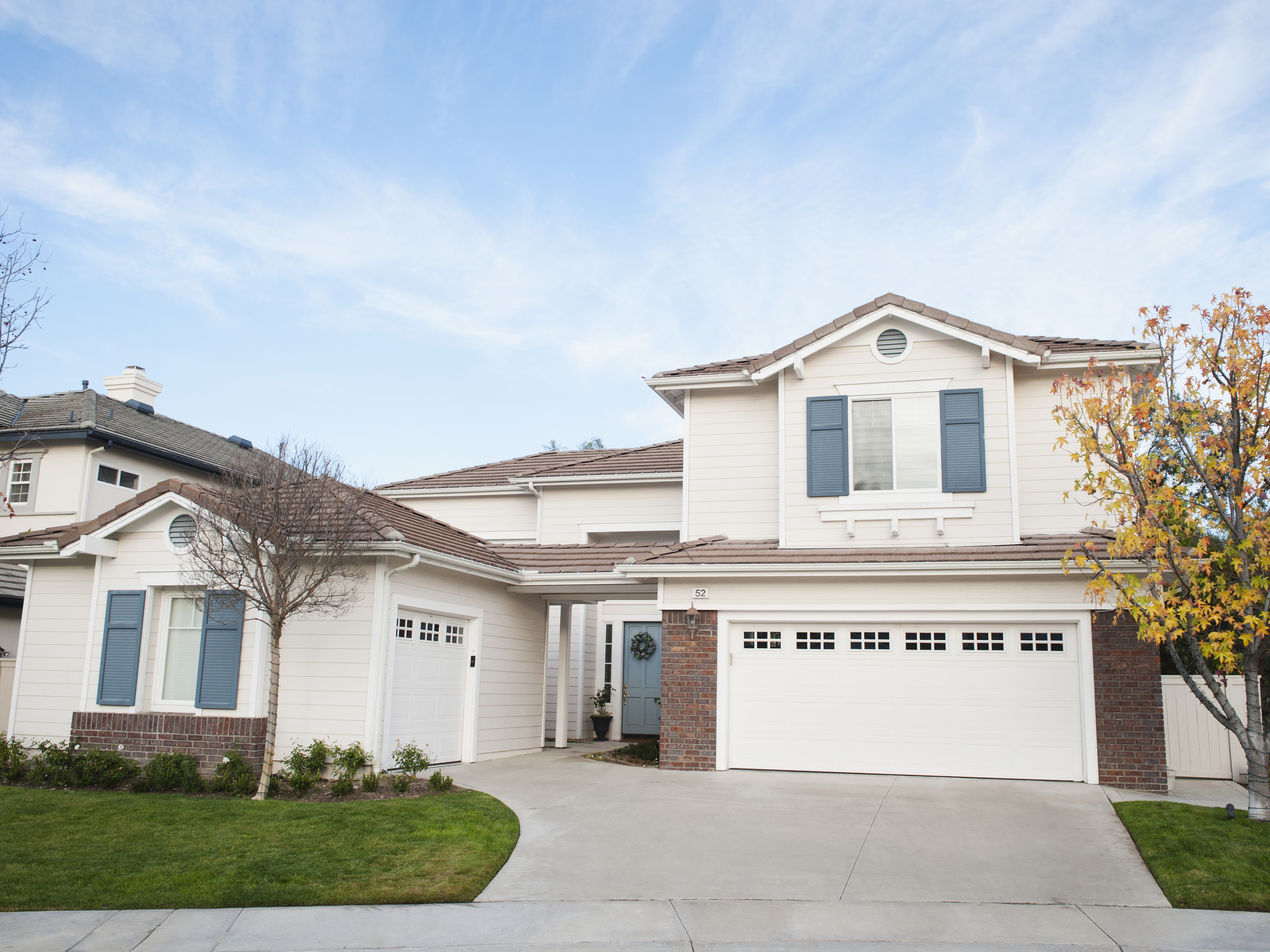 A modern suburban two-story house with a double garage, front lawn, and a single tree on the right side