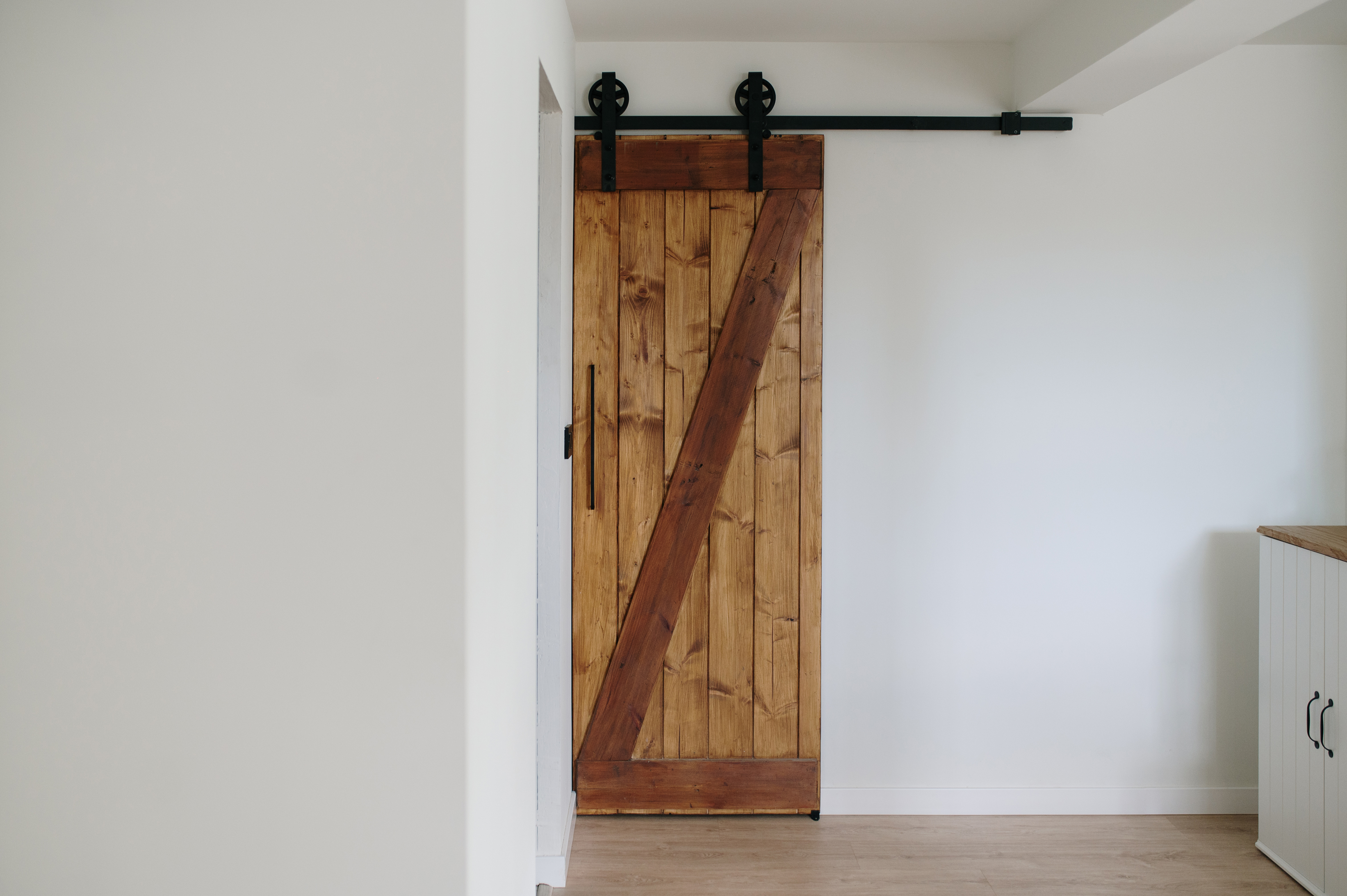 A rustic wooden barn door with a V-pattern, mounted on a black sliding track, installed in a minimalist room