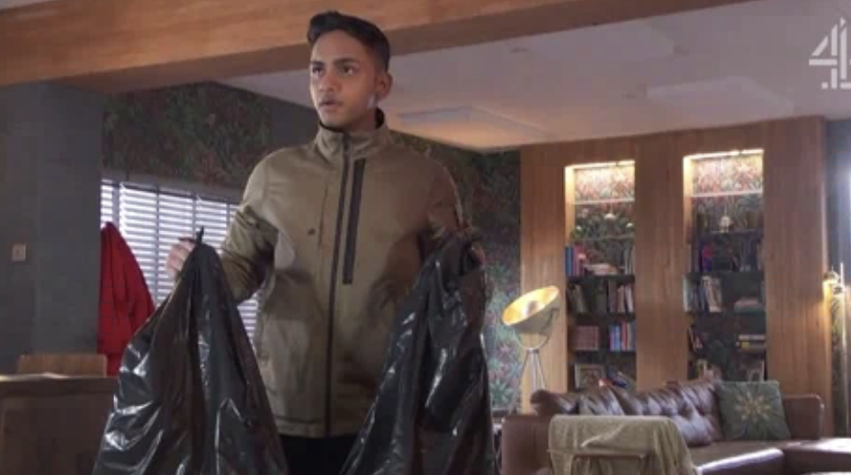 A man is seen in a living room holding two large garbage bags. The background shows a modern, well-decorated home with a bookshelf and floor lamp